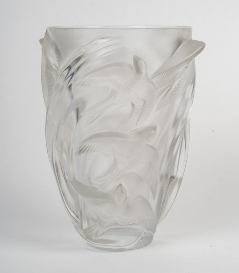 Translucent glass vase decorated with swifts in flight, arranged in an ascending spiral. The birds are depicted in high relief, their outstretched wings creating a dynamic and fluid impression around the vase. The surface alternates between