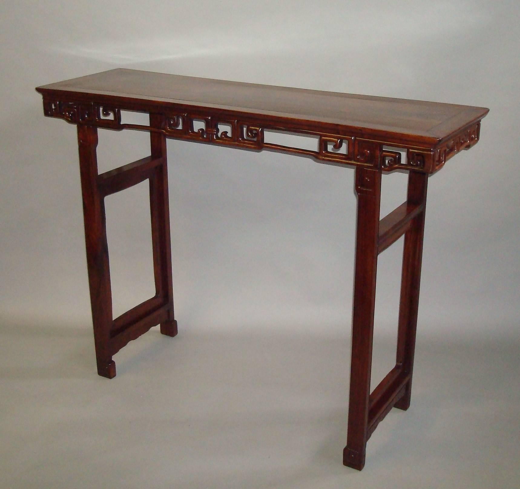 A good 19th Century Chinese Hongmu alter table; the well figured rectangular top of traditional cleated form above a carved and pierced archaic frieze, raised on moulded legs headed with carved scroll decoration. Housing shaped open end panels with