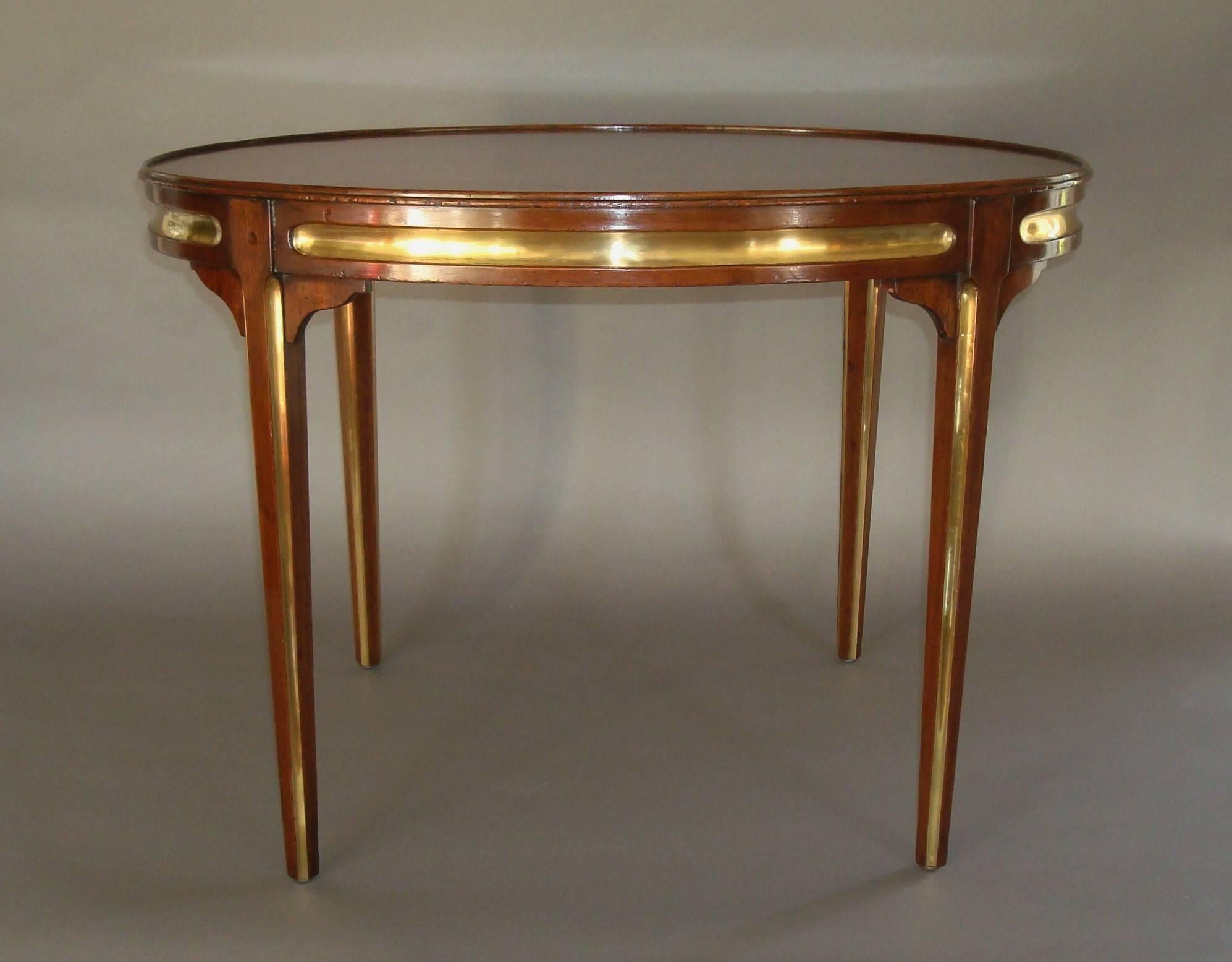 Early 20th century oval mahogany and brass low occasional table, the oval mahogany top with a thin raised moulded edge above a shallow frieze with fluted brass panels around; the square tapering legs headed with scrolled corner brackets and tapering
