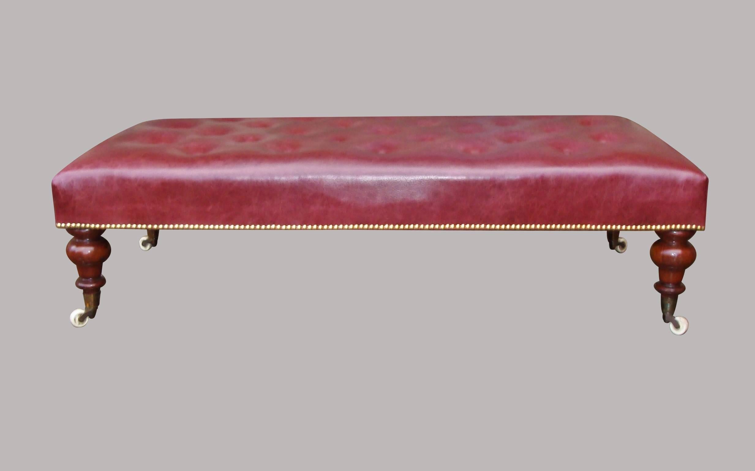 19th century large mahogany and leather low stool; the rectangular padded seat, newly upholstered in the traditional manner in good quality burgundy hide with a buttoned top and close brass studded edges; raised on turned tapering mahogany legs