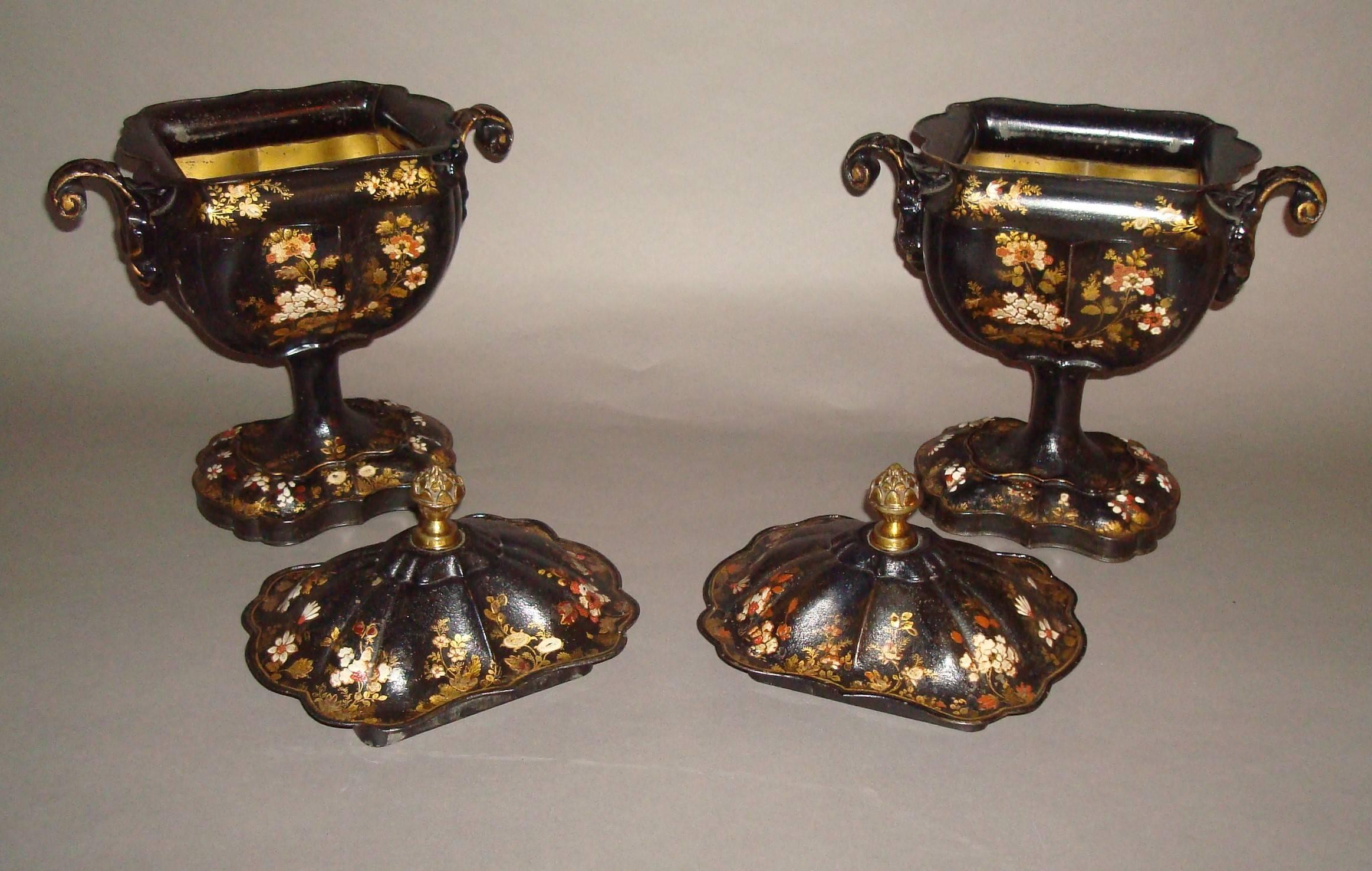 A good Regency pair of tole chestnut urns of unusual design; the scalloped shaped rectangular lids with an ornate brass finial above the shaped urns with acanthus scroll side carrying handles, supported on a similarly shaped plinth. All finely