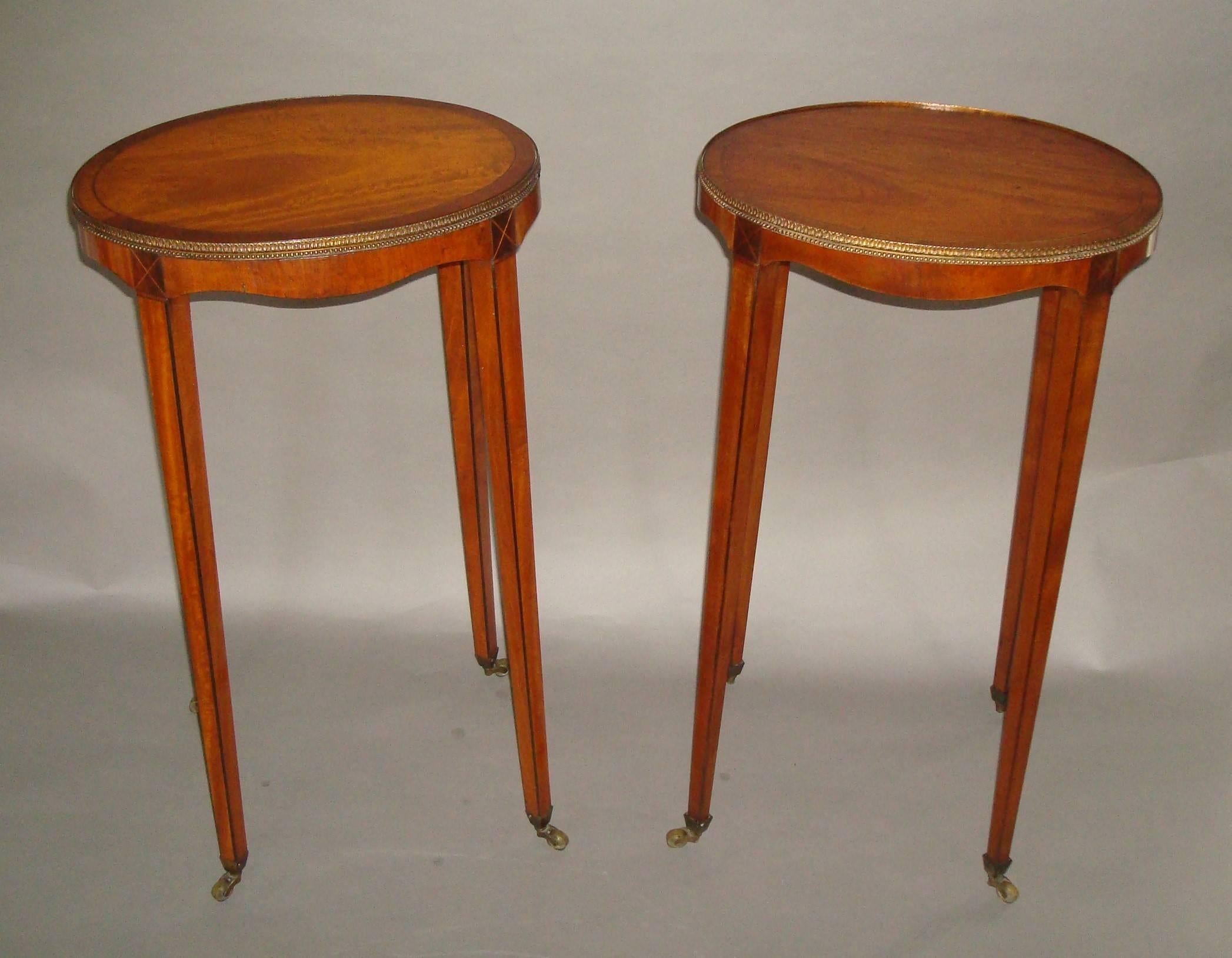An elegant George III matched pair of satinwood urn stands; the figured oval tops with ebony and boxwood stringing crossbanded in tulipwood, surrounded by gilded brass bead and foliate design moulding, above a shallow swept apron raised on square