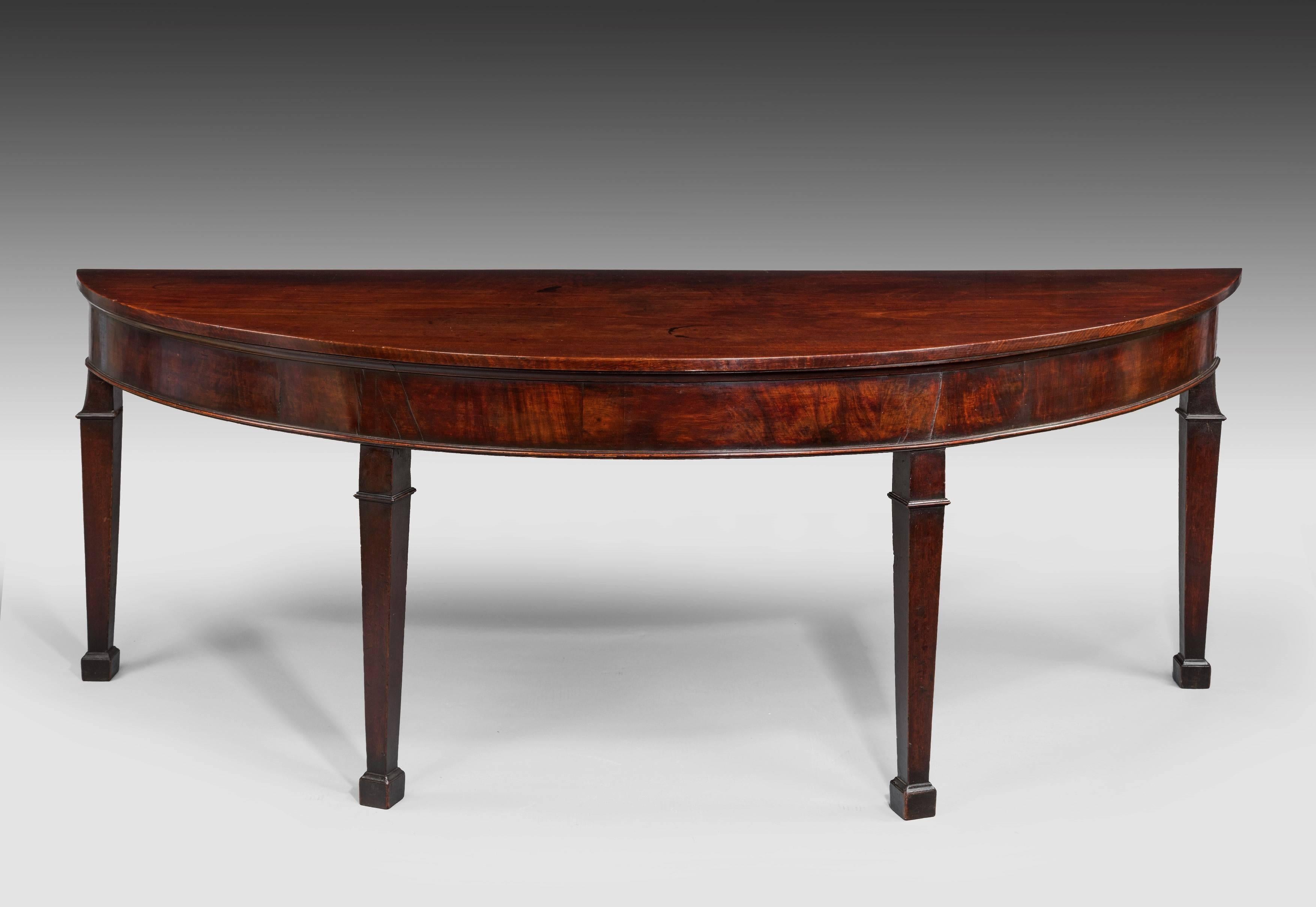 An impressive Georgian mahogany Irish demilune side table of large proportions, the figured demilune top of great colour and patination above a cavetto moulding; the figured mahogany frieze with a slender moulded edge, raised on square tapering legs
