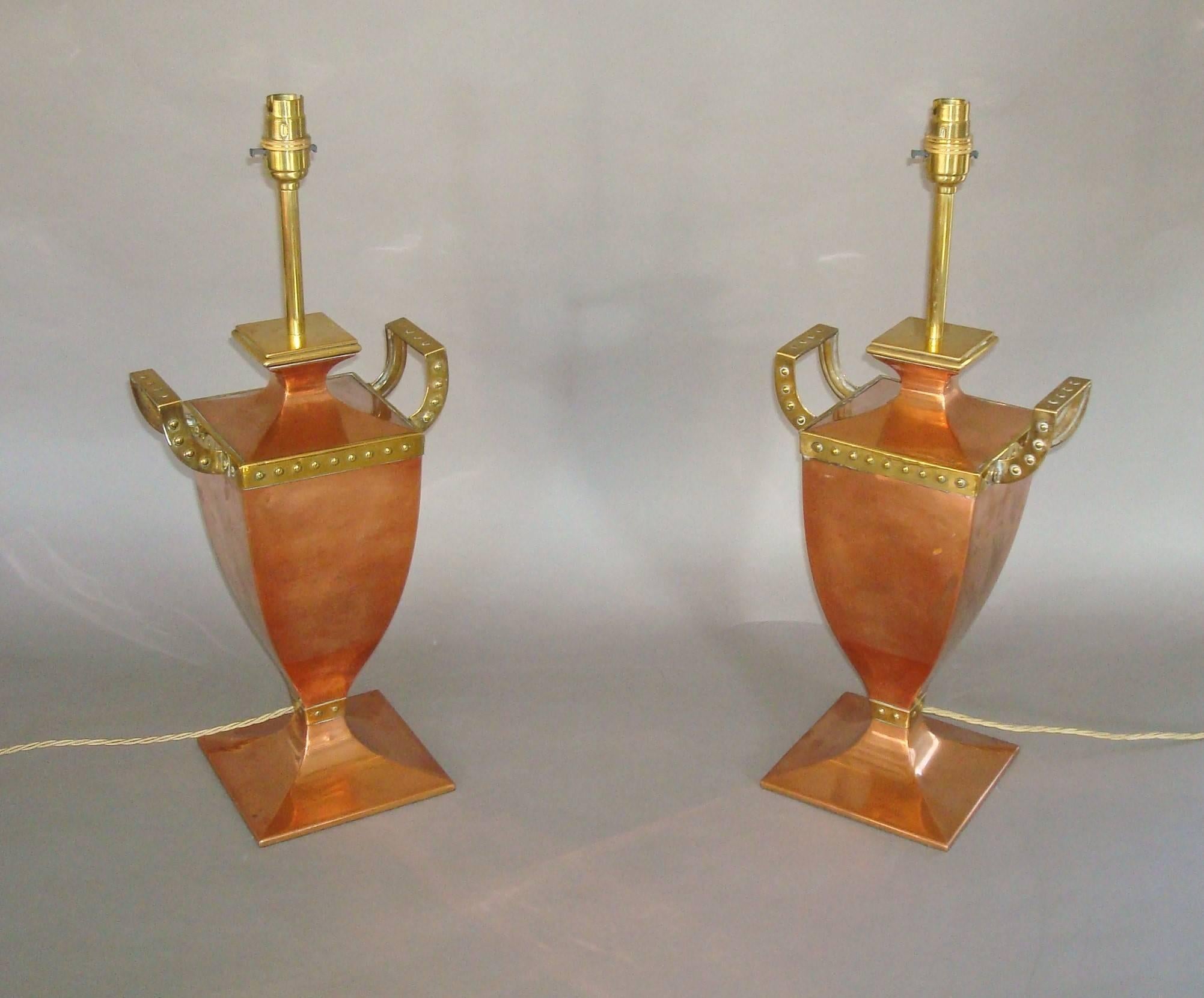 Stylish early 20th century pair of copper and brass lamps of unusual form; the copper urn shaped bodies with square flared bases and brass riveted mouldings with raised shaped carrying handles to the sides,
English, circa 1920.
Good condition