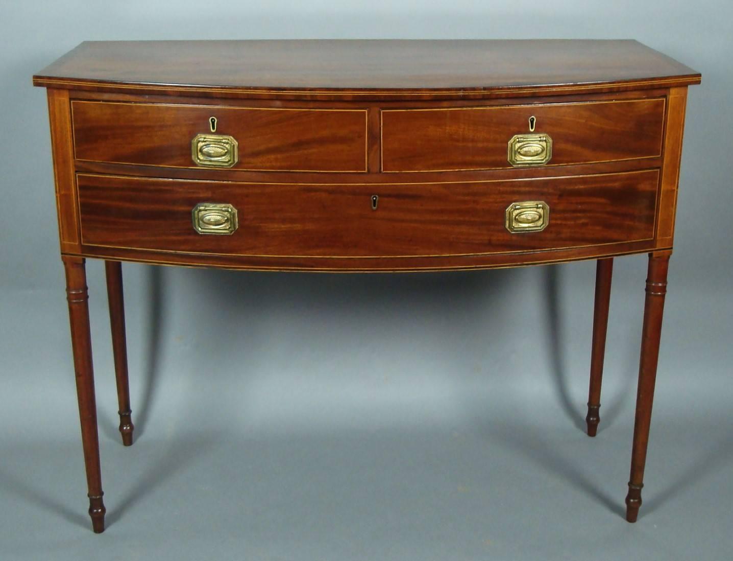 George III mahogany Sheraton bow fronted side table of elegant proportions, the well figured mahogany top with double stringing and crossbanded border above two short and one long drawer having oak drawer linings and original gilt brass handles,