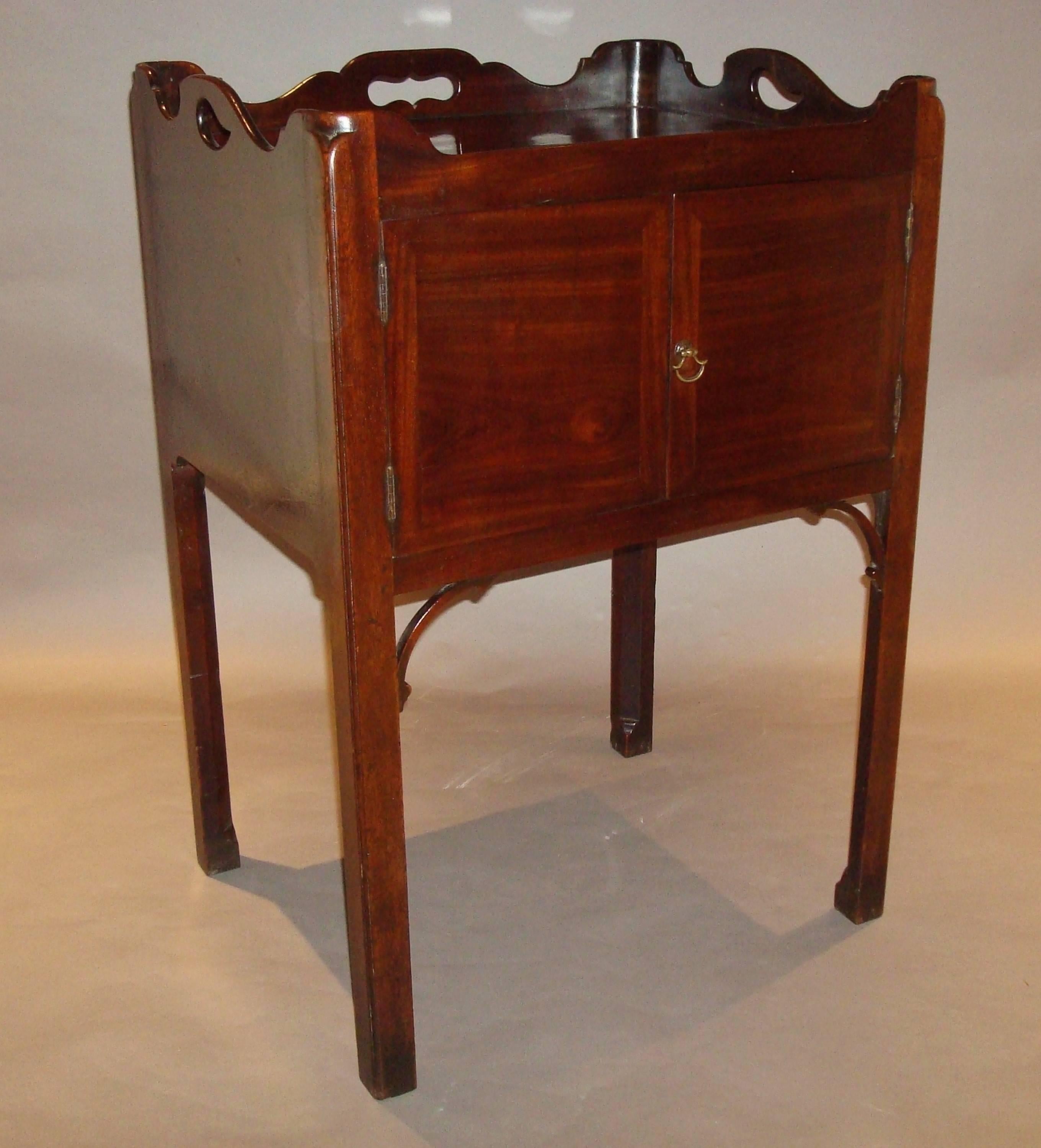 An excellent example of a Georgian mahogany 'Chippendale' tray top bedside cabinet. The well figured top with exaggerated shaped three quarter gallery incorporating pierced handle grips, supported in re-entrant shaped cornered uprights. The well