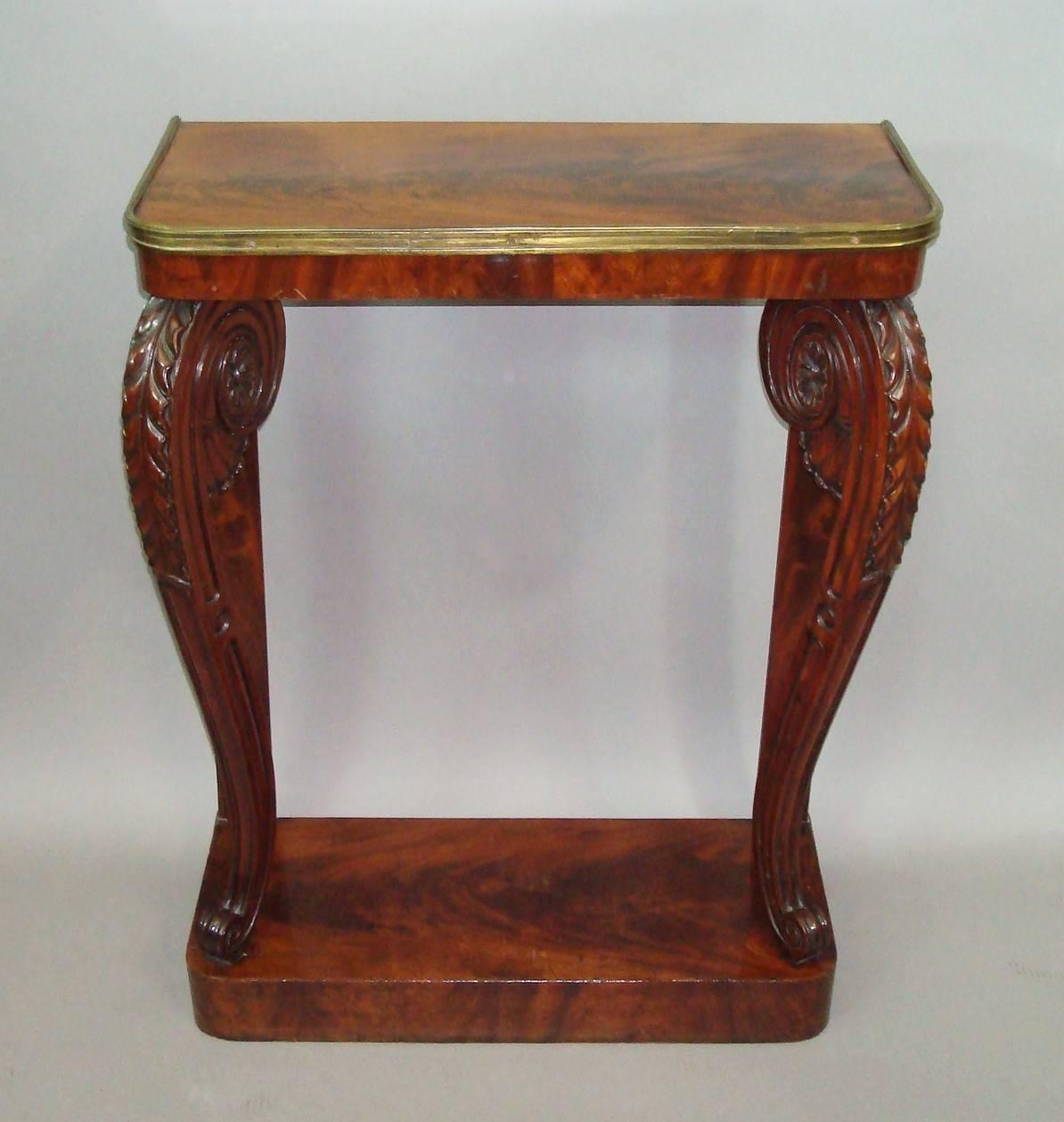 Good Regency figured mahogany console / pier table of narrow proportions; the well figured mahogany rectangular top with curved front corners and a brass moulding to the edge; raised on exaggerated scrolled legs with bold acanthus carving with fans