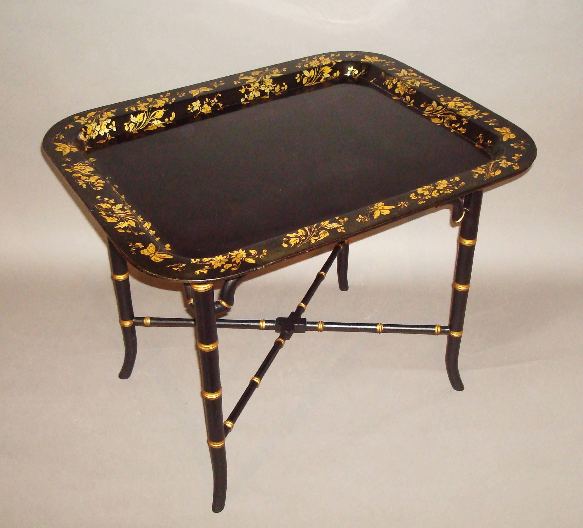 Good English Regency papier mâché tray on stand; the rectangular tray with a raised border finely decorated in gilt with floral sprays and various butterflies. The top fixed to a good quality custom-made later Stand of faux bamboo design with shaped