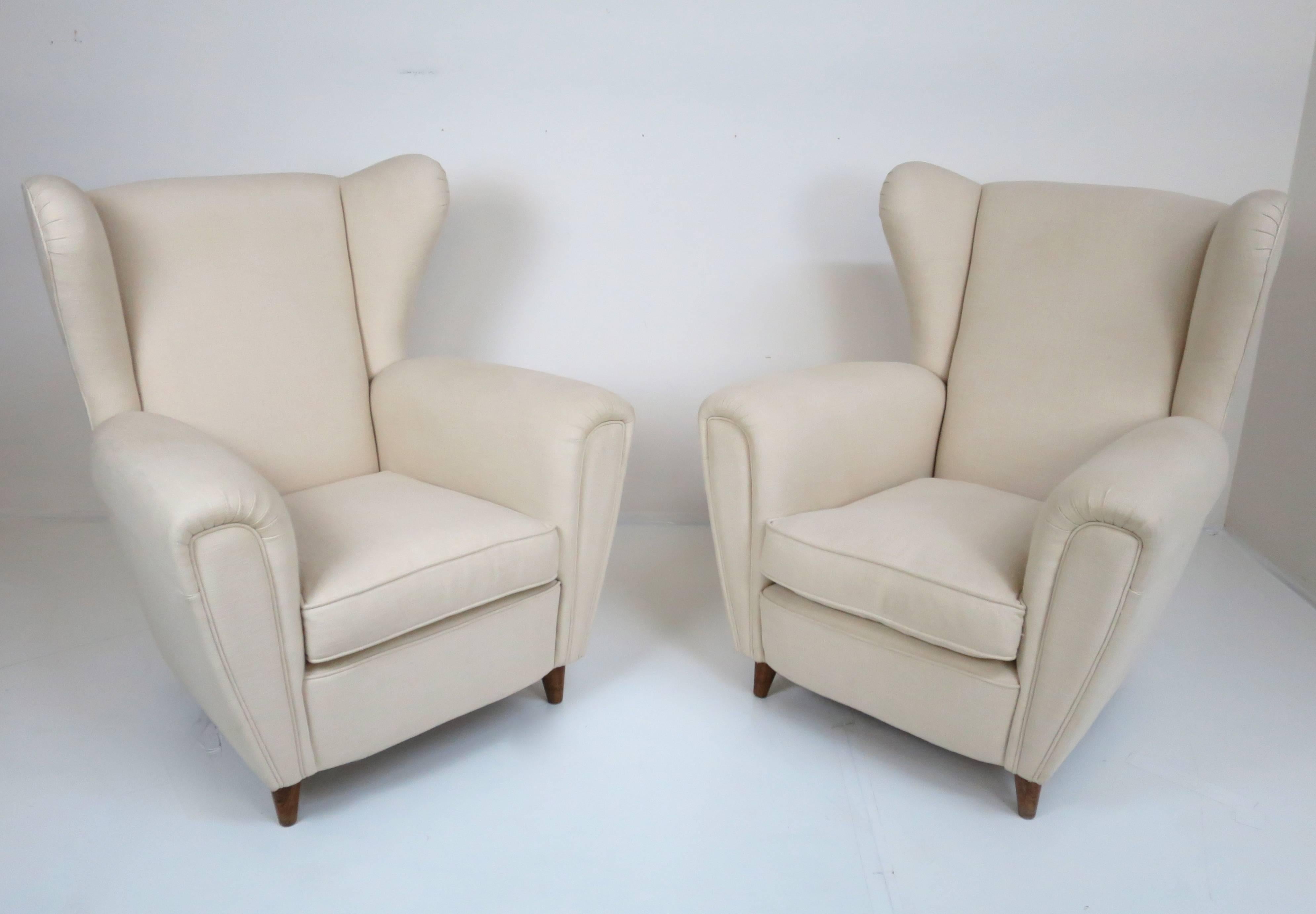 Stylized Italian wingback pair of large chairs, circa1949. Reupholstered in cream linen with original down seat cushions. This pair of Italian chairs is large-scaled and will work well with contemporary furnishings as well as vintage, which is not
