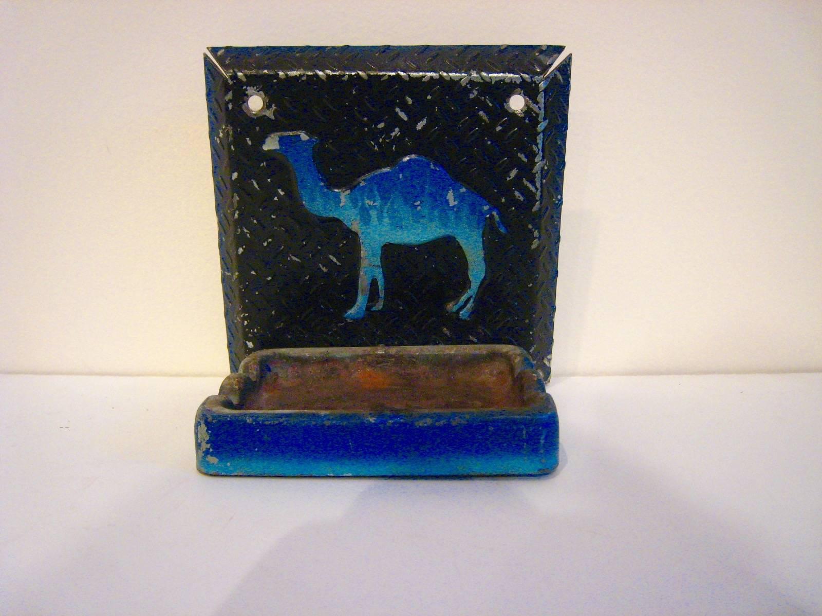 A striking wall-mounted metal and ceramic ashtray with beautiful image of the Camel Cigarette logo. Ashtray is easily affixed to the wall with two screws and the ashtray flips over to empty. Unusual piece.