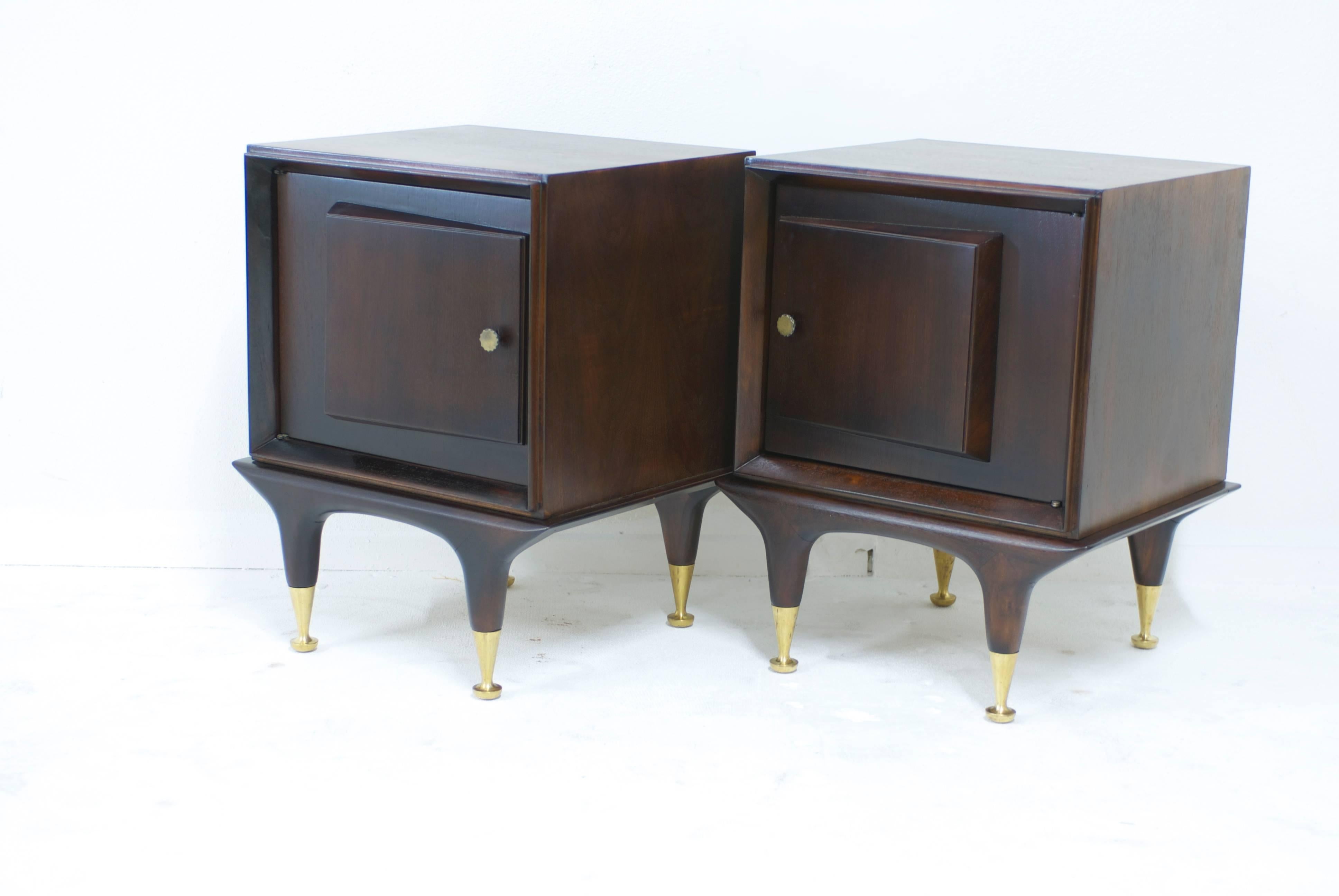 A sculptural pair of Mid-Century bedside cabinets made of mahogany.
The cabinets have a door set on an angle for visual interest giving them a cubist feeling. The nightstands retain all of their original hardware including the brass sabots on the