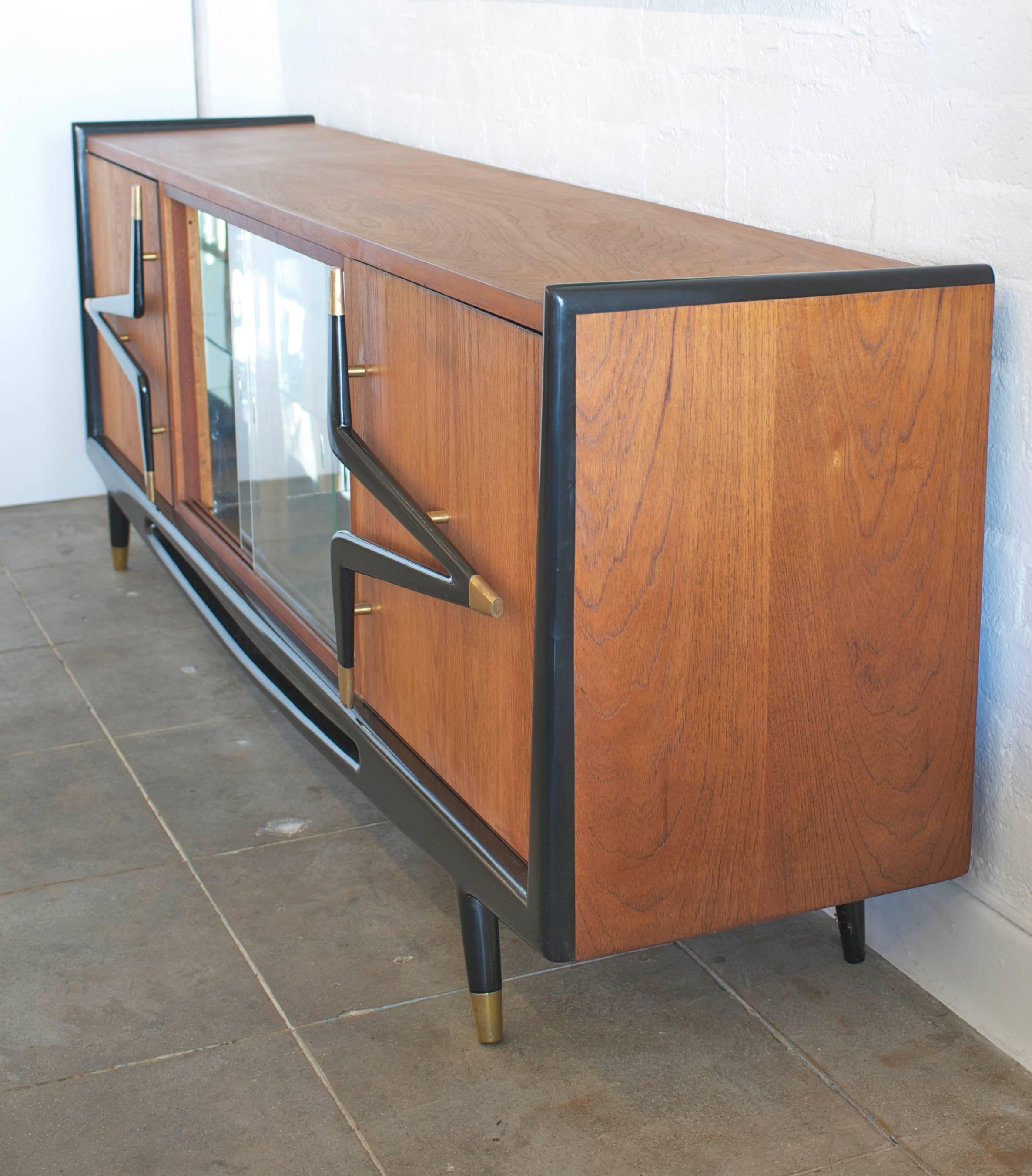 Made of mahogany, ebonized wood, mirror and brass this Mid-Century cabinet designed by Eugenio Escudero of Mexico has beautiful lines. At just over 8 feet long this sideboard or dry bar is substantial in scale. The hardware is bold, graphic and