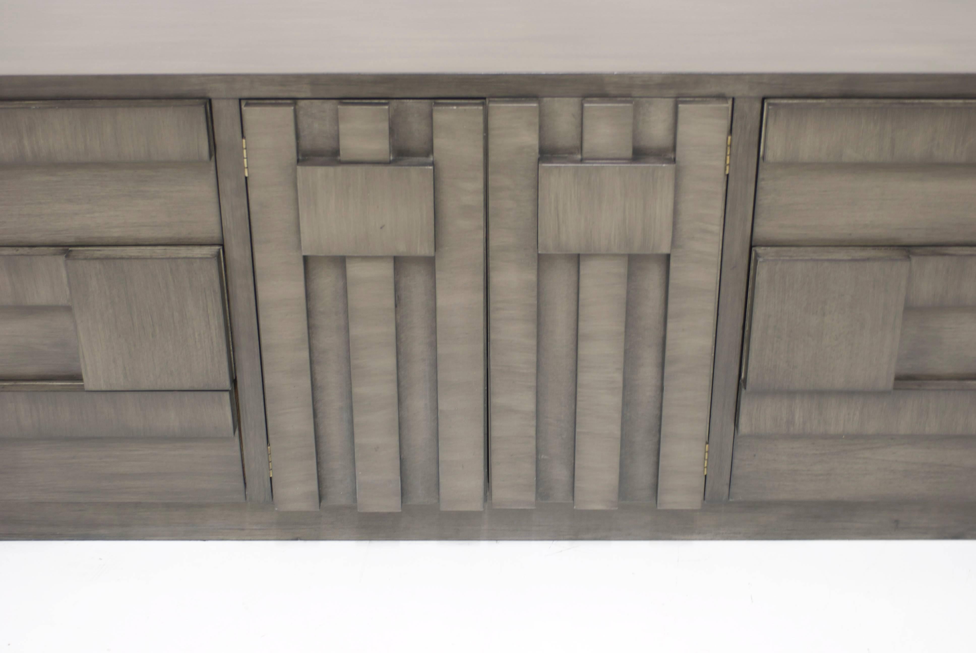This dresser or sideboard manufactured by Lane has a handsome geometric pattern on the door and drawer fronts. It has been refinished in a multilayered charcoal grey finish which has a ashy grey undertone and then a brushed stain of charcoal layered