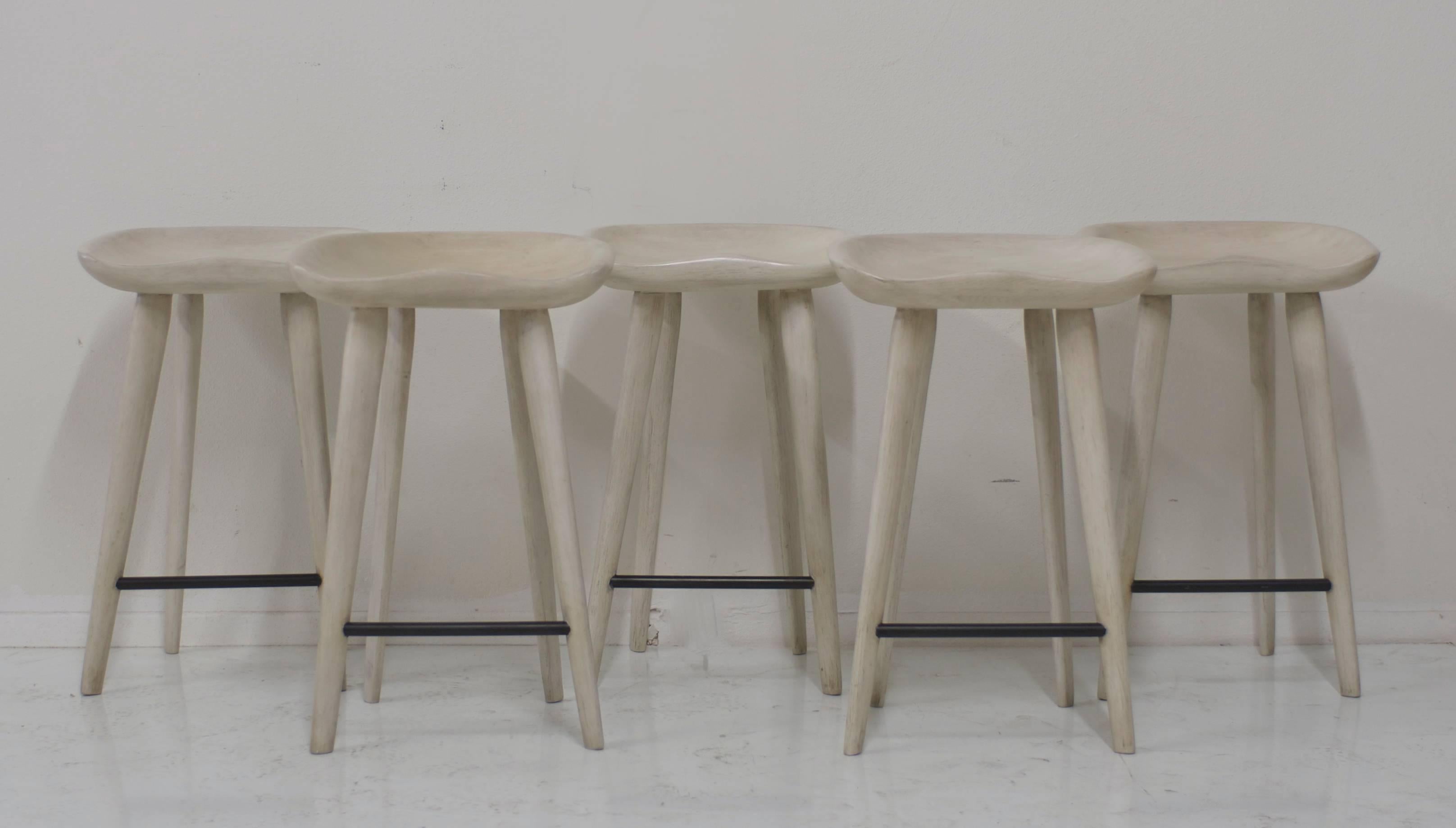 A set of five bar stools that have a customized finish that has a mix of cream and layers of grey and beige colors which blend together to look like driftwood. The footrests are a charcoal black.
There is some natural variation in the colors that