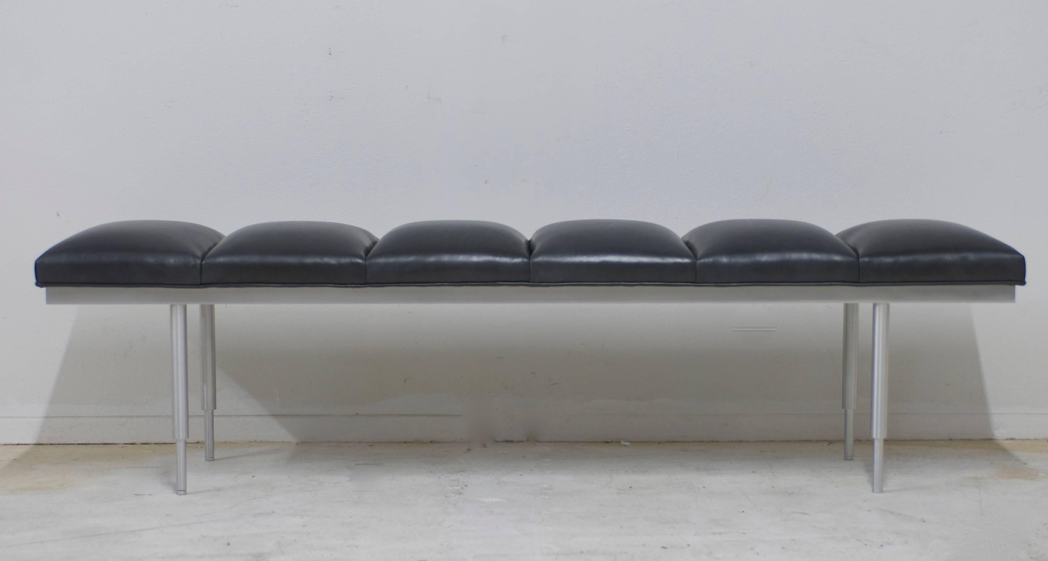 A  brushed aluminum, 1970s era bench that has been reupholstered in a black charcoal leather with a slight metallic sheen to it. The leather is channel tufted for a sleek Classic modern look. The legs of the bench have two placement options they can