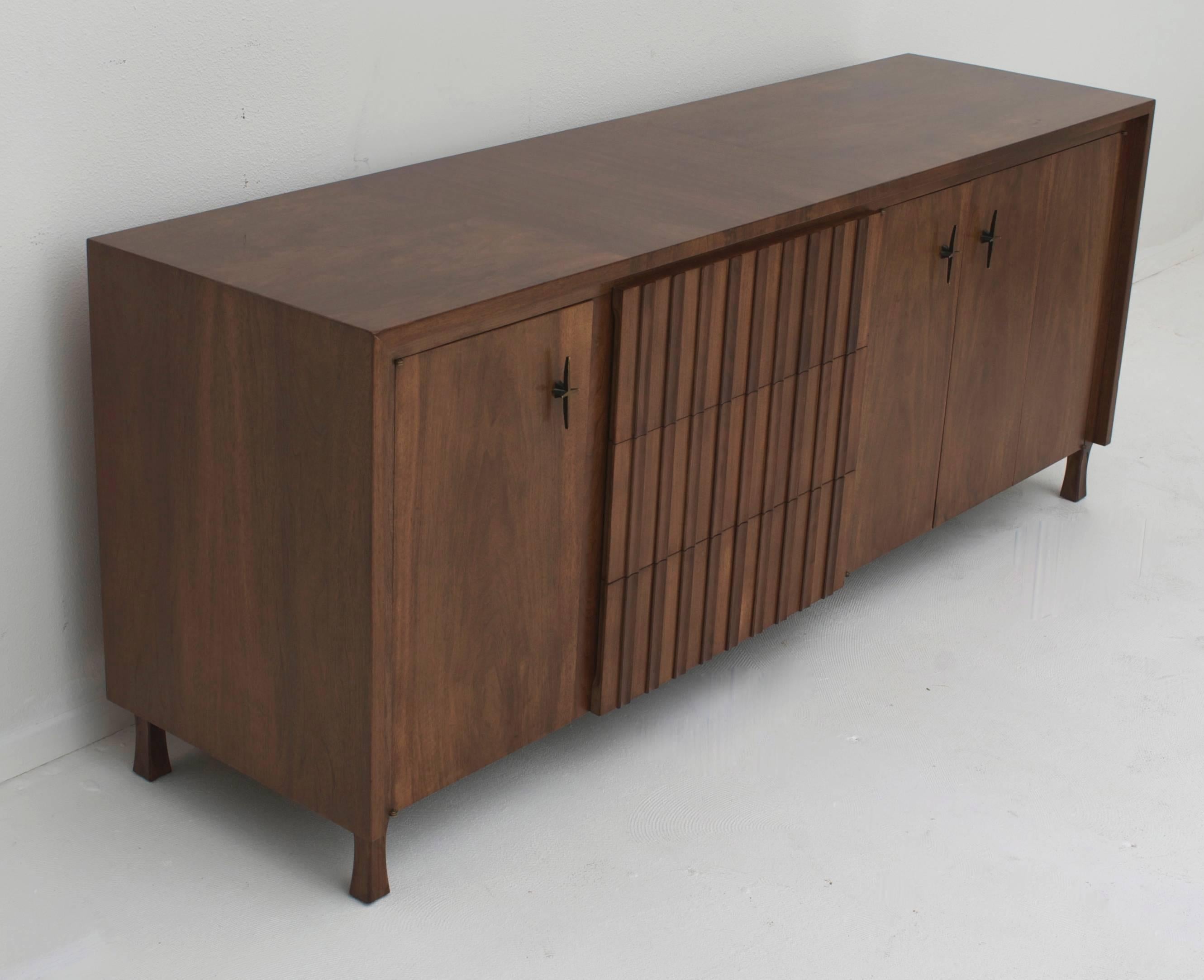 A solid walnut credenza which has been restored to its original luster. It retains its original hardware.
The cabinet has a fixed door and a set of accordion doors on the right side which open to reveal a shelf. The middle has three fluted front