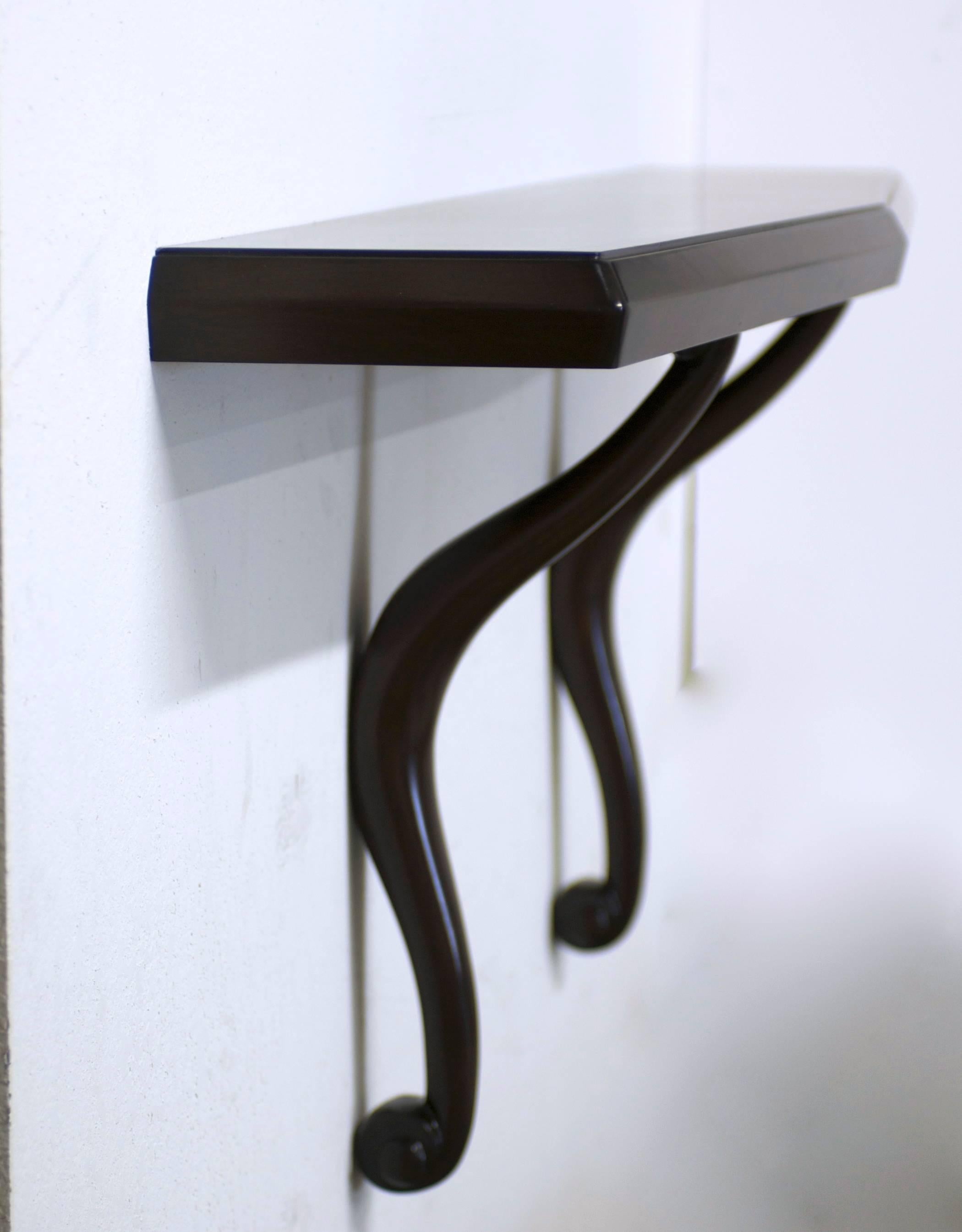An elegant wall-mounted console made of mahogany. There is a thin inlay of dark ebonized wood on the top. The carved scroll supports gracefully rest on the wall. The console has hidden support pegs that screw into the wall. The shelf profile is 2