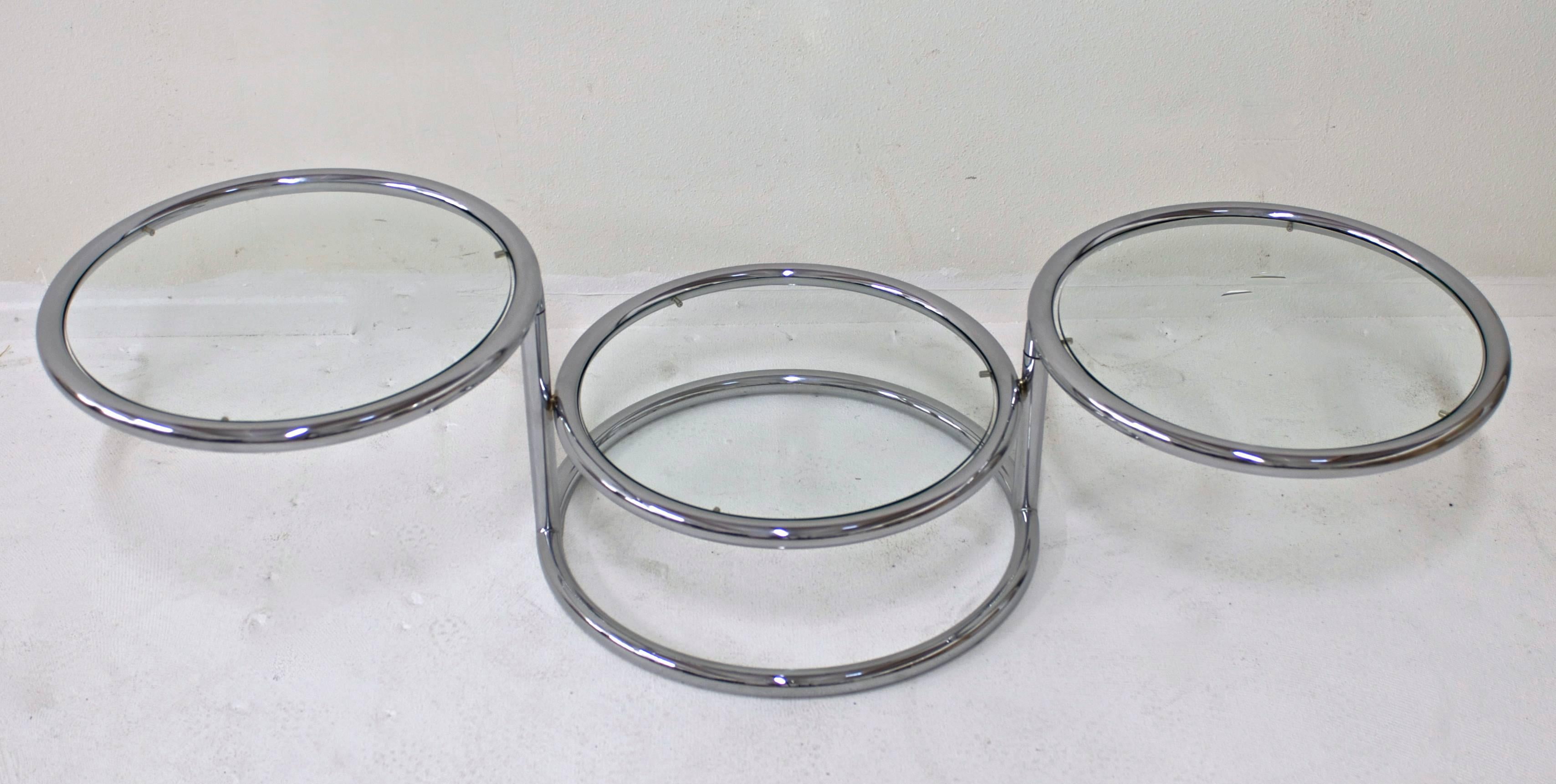 A tubular chrome table that has three glass tiers. The top two can pivot left or right to make a larger cocktail table and when closed it compacts to 24