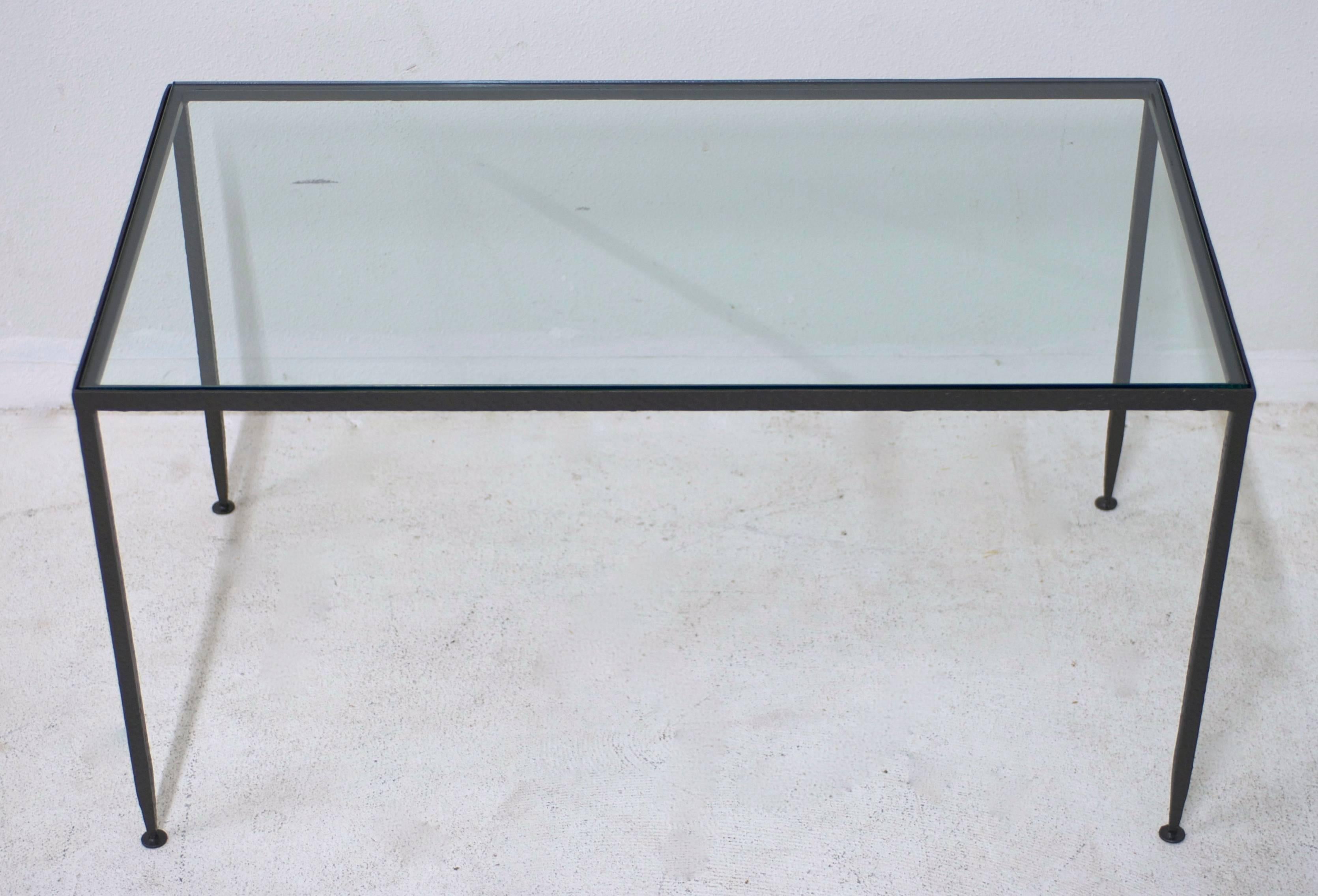 This hand-forged wrought iron and glass top coffee table has a hammered textured finish to the iron. The thin legs taper elegantly. The glass is new and therefore in excellent condition.