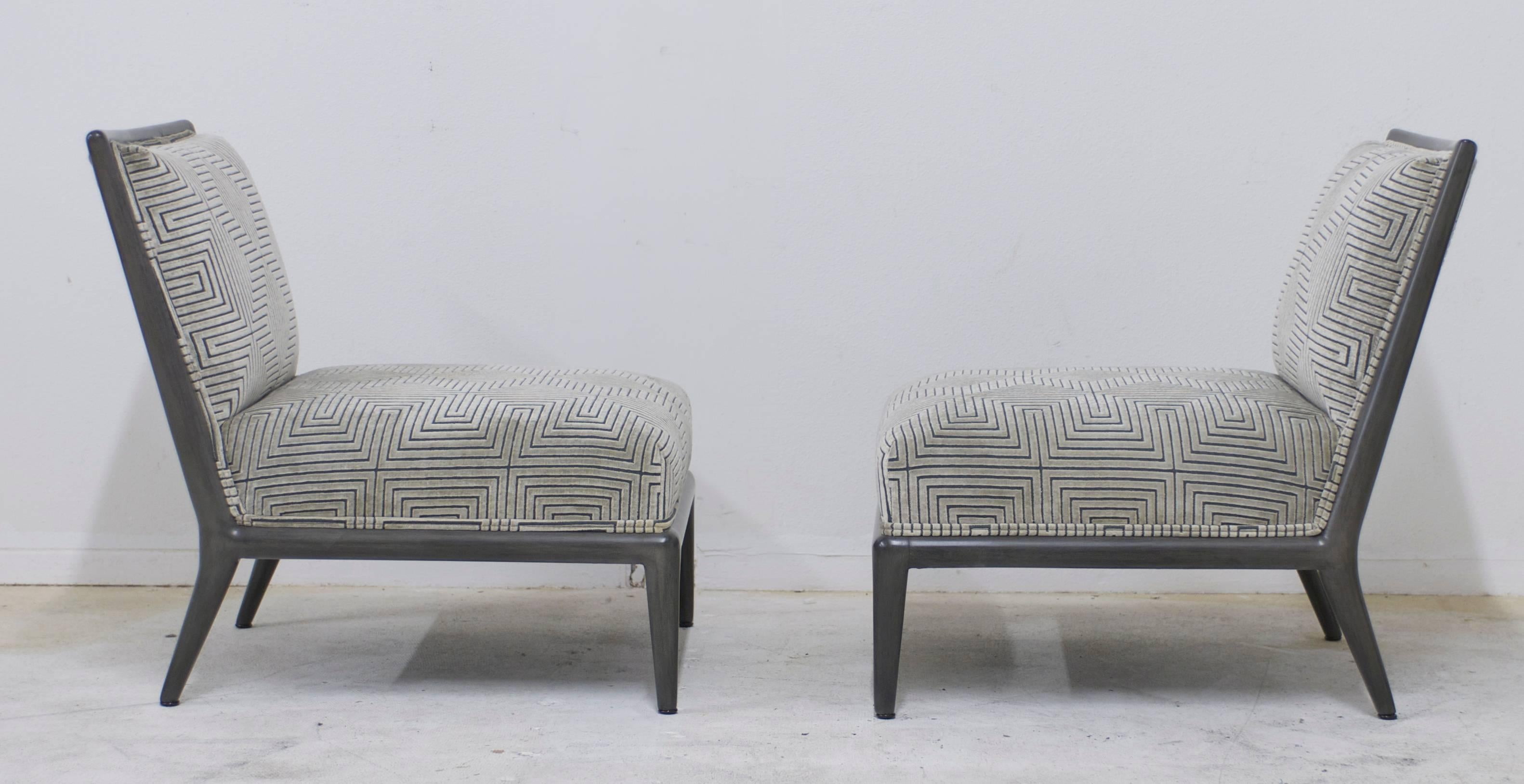 This pair of low slung Mid-Century slipper chairs have had their frames refinished in a deep charcoal grey finish that has a brushed stain layered on top to give the finish depth. The uphostery has been redone in a geometric cut velvet pattern that