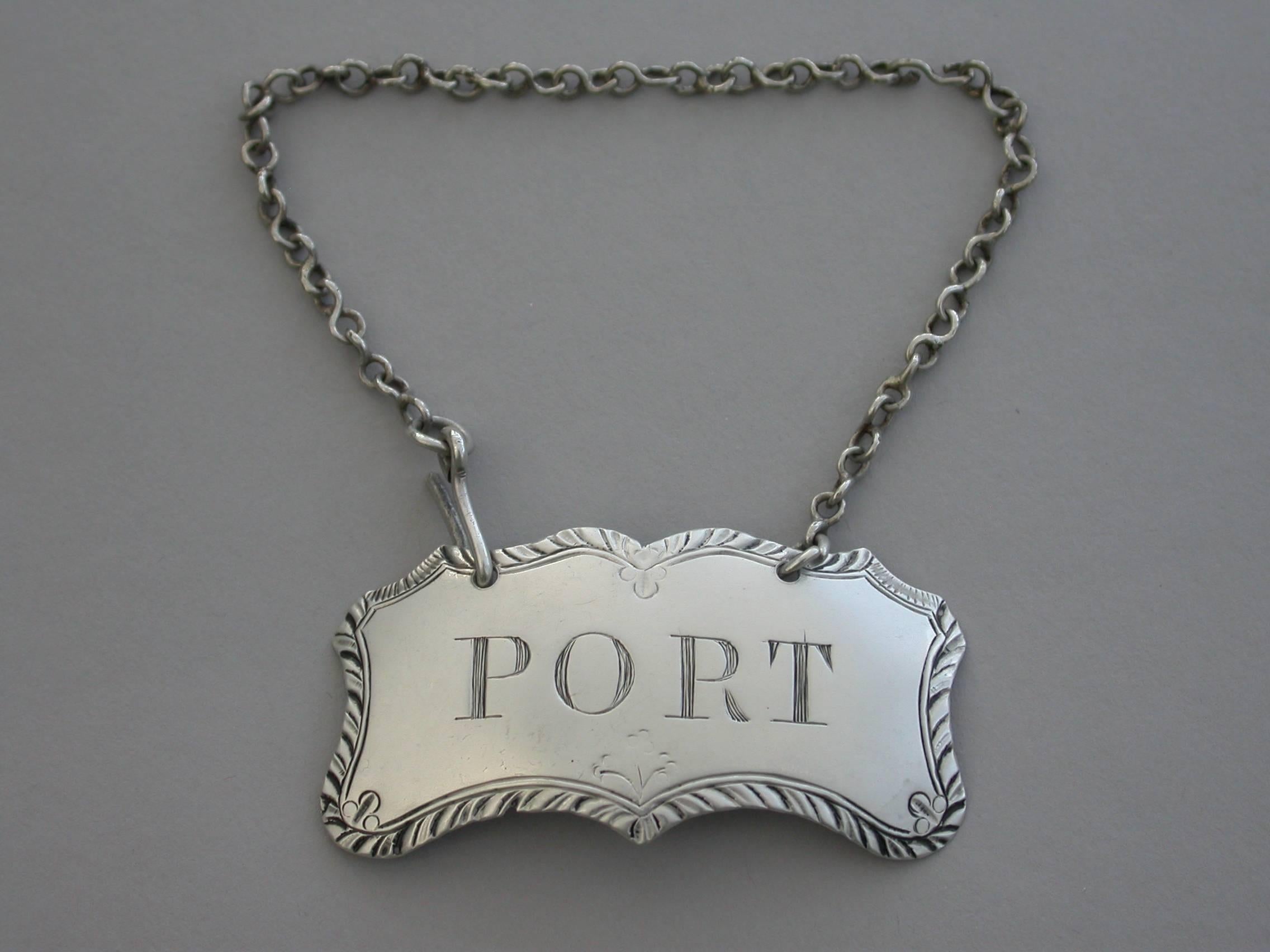 An unusual George III Irish silver Wine Label of shaped rectangular or cartouche form with feather edged border and engraved floral devices, incised for Port.

The suspension chain attached with a scrolled clip to one end (typically