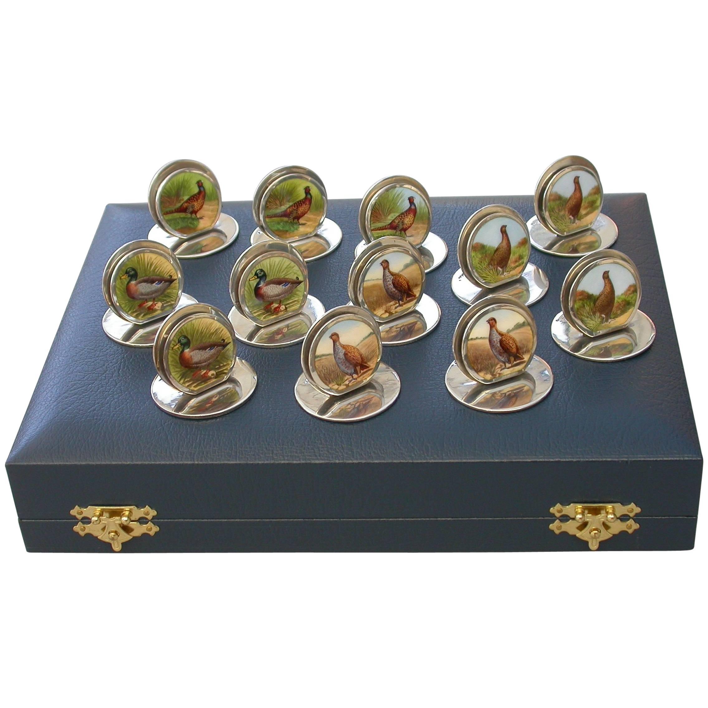 A superb composed set of 12 cased Edwardian silver and enamel game bird menu holders, of sprung double-disc form on flat circular bases. The faces finely enameled with portraits of cock pheasants, drake mallard, English partridge and red grouse. All