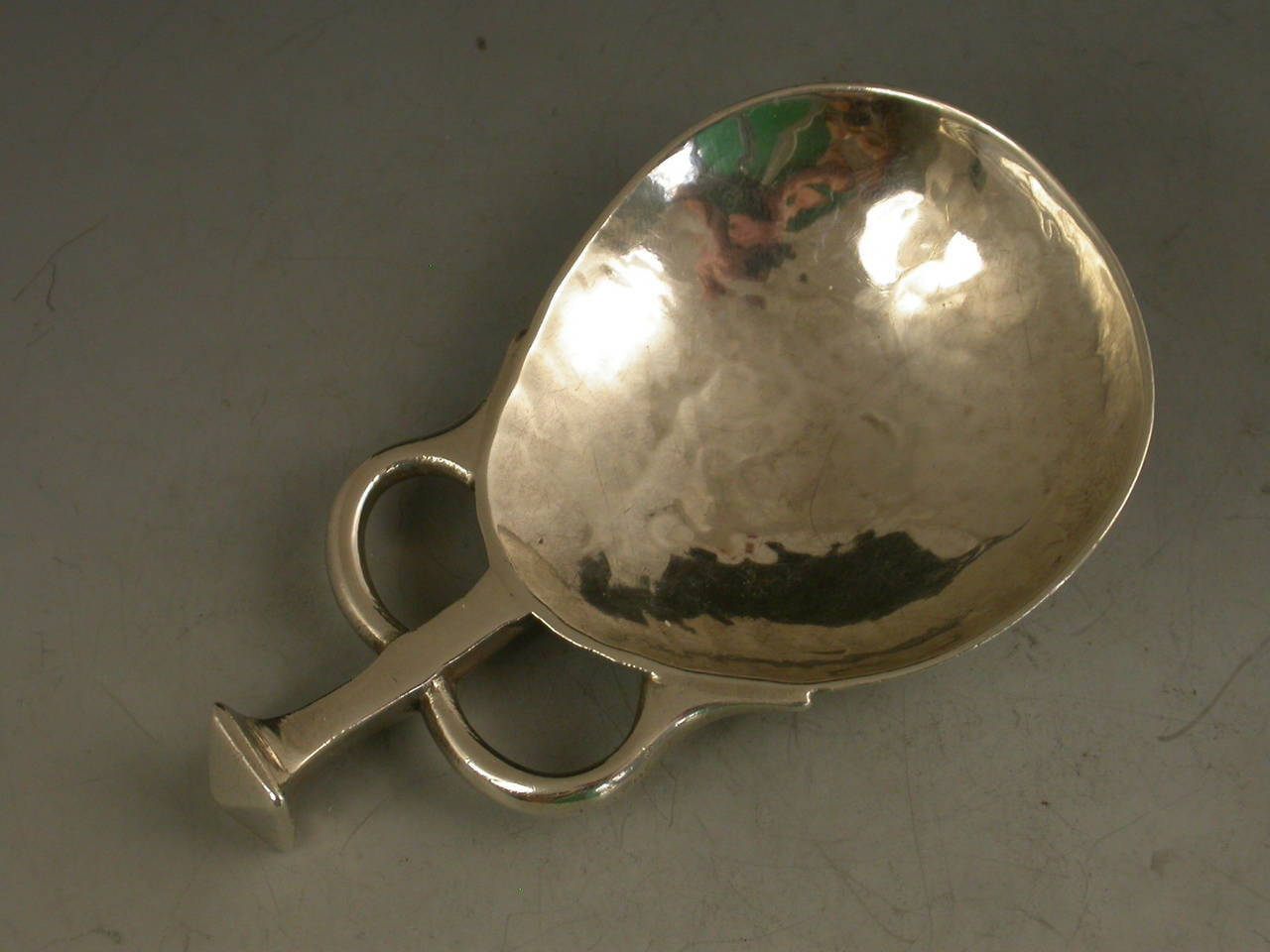 A good early 20th century silver caddy spoon made in the Arts & Crafts style with hammered pear shaped bowl and seal capped square handle with looped supports. 

By A E Jones, Birmingham, 1919

In good condition with no damage or