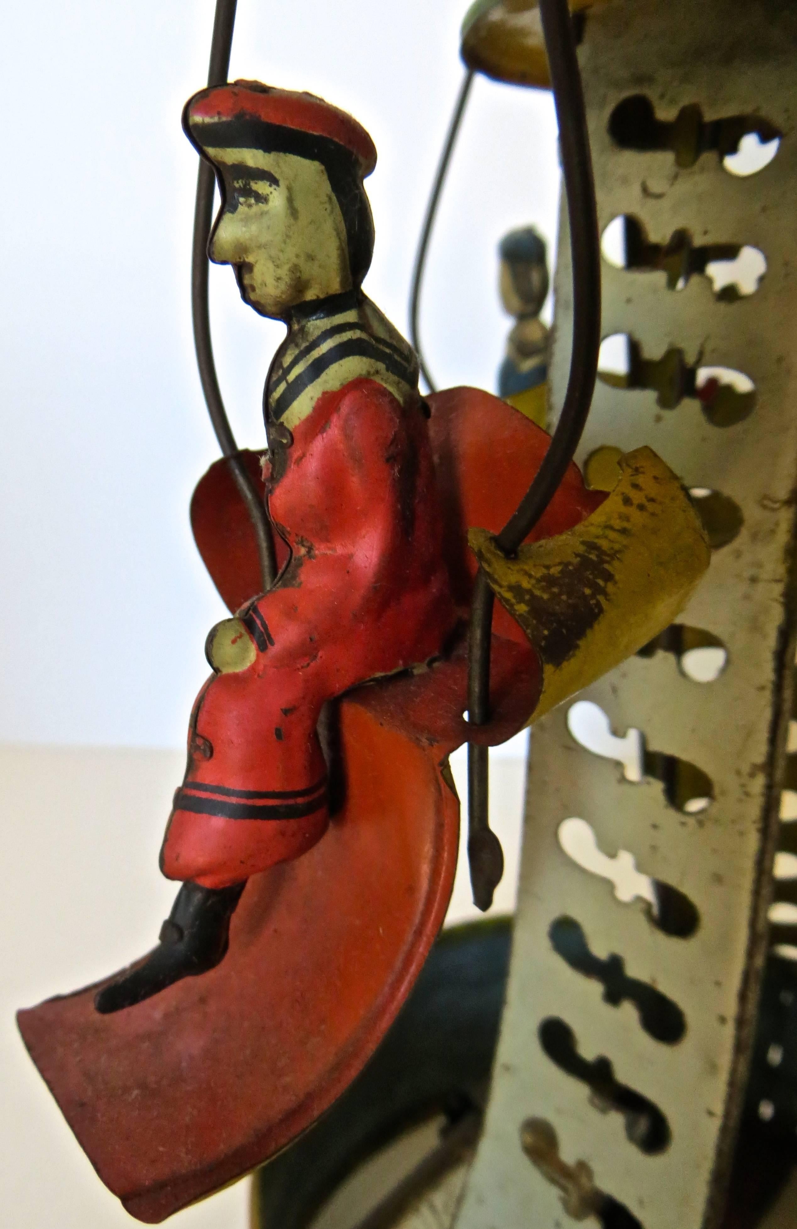 American clockwork Carousel Toy made of tin; hand-painted in bright colors of reds, green, yellow, and blue. Wind-up mechanism is in perfect working condition and carousel goes round and round for quite some time. The hand-painted canopy top