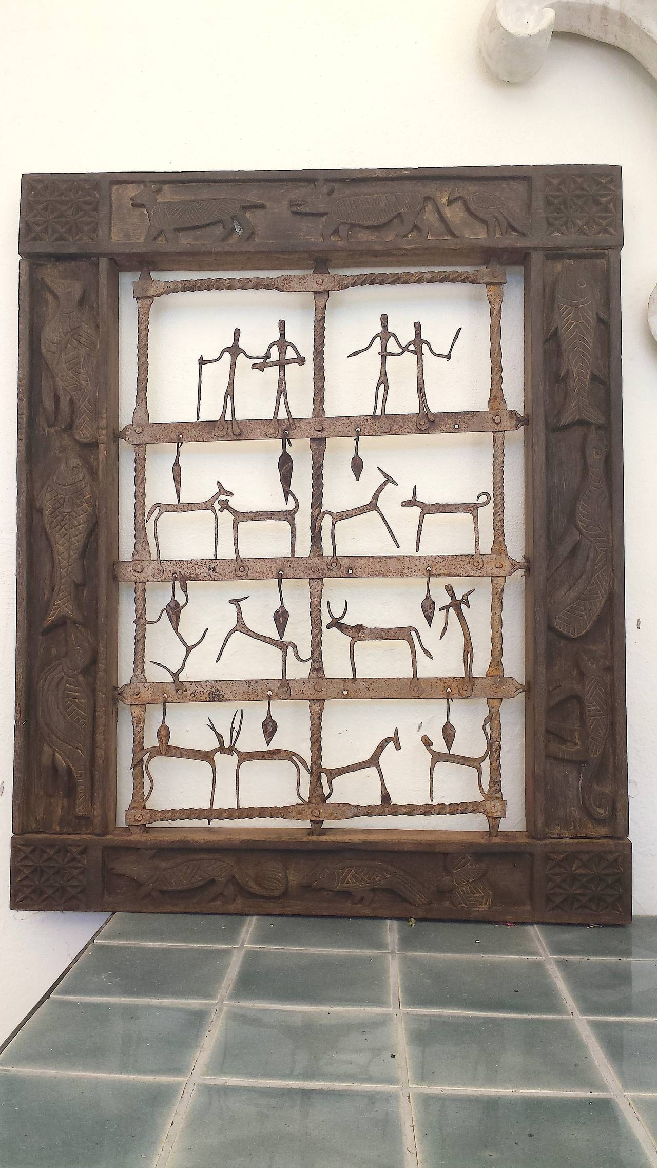 Stunning unique complimentary pair of Indonesian ethnographic architectural 'windows' wall panels with dark wood frame with carvings of fish, big cats, birds, turtles surrounding a rusticated metal grid with figures and animals and hanging