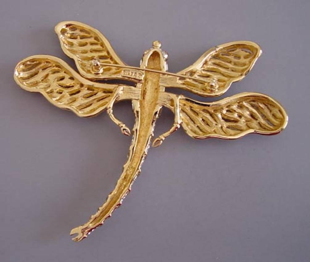 A 1980 quality Runway Ciner  articulated dragonfly-gold heavy plated base metal with a multitude of Rhinestones, red cabochon eyes. Ciner label en verso.
A stunning eye-catching piece.

Ciner Jewelry Company, begun in New York in 1892 by Emanuel
