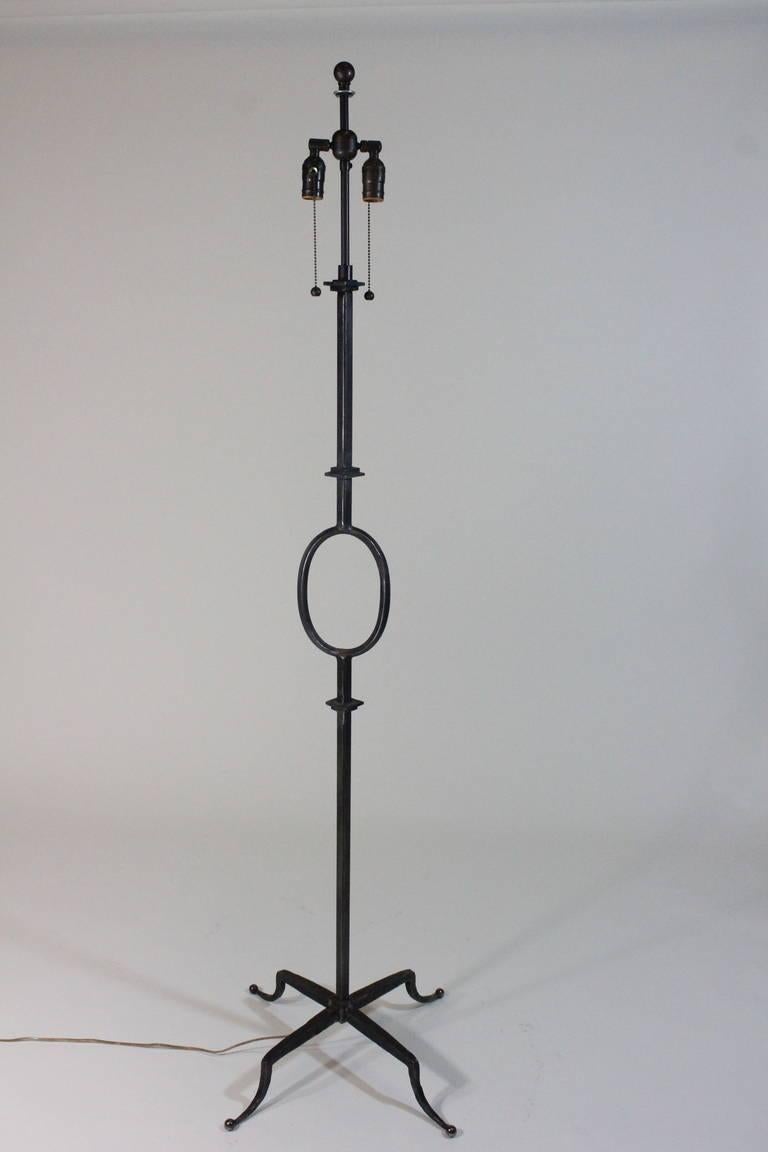 A superb design attributed to Poillerat and manufactured by Mattaliano. Hand-wrought iron floor lamp with an oval shape feature detail, in blackened wrought iron finish, with a double two lamp holder and iron finial. Dark gray linen shade in shape