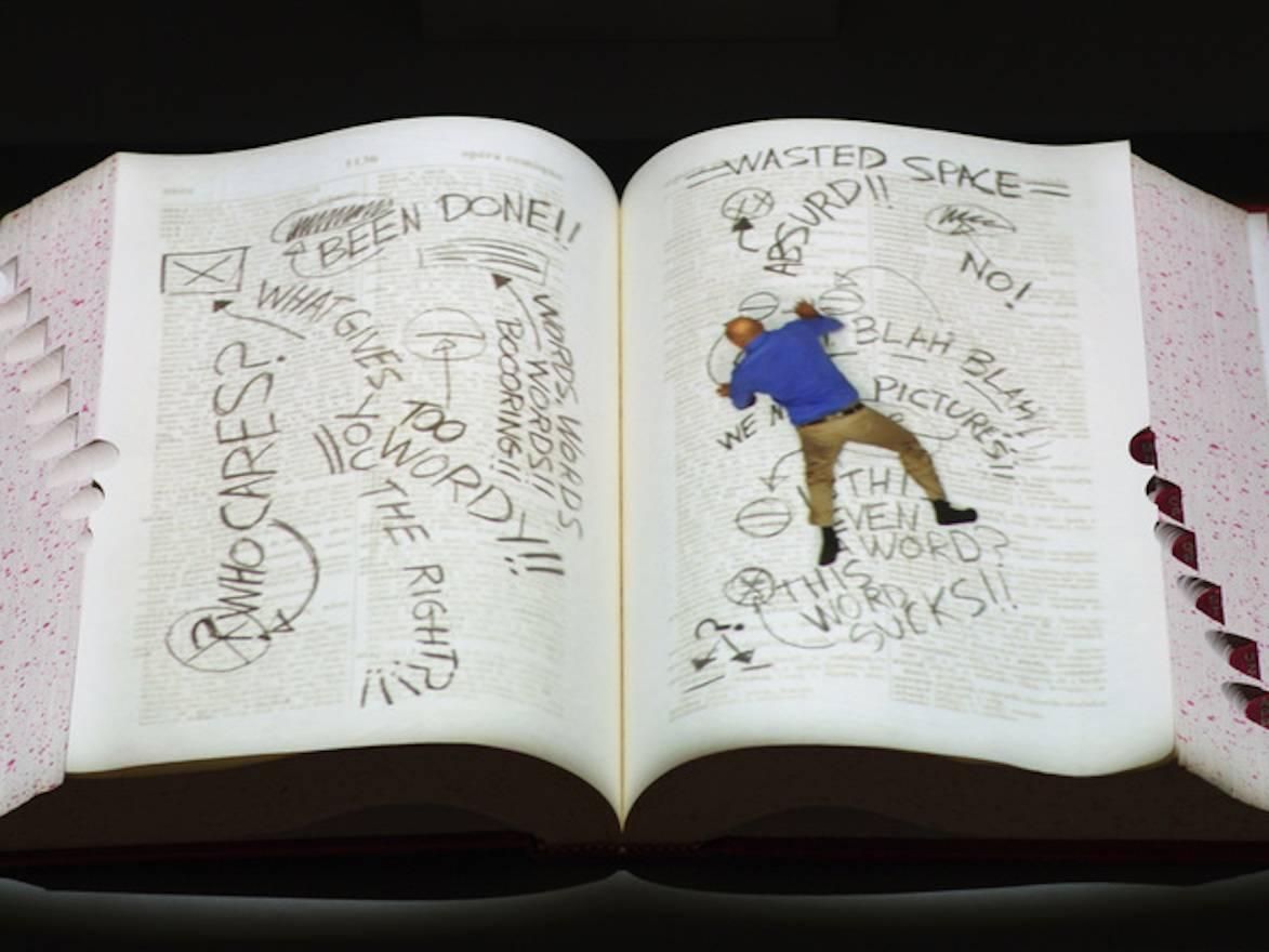 Artwork by important video artist Peter Sarkisian.  A Video with audio is projecting on a blank open book--You will see in the book, a small man crawling about going in and out of the binding while rewriting a dictionary.  Sarkisian's idea is