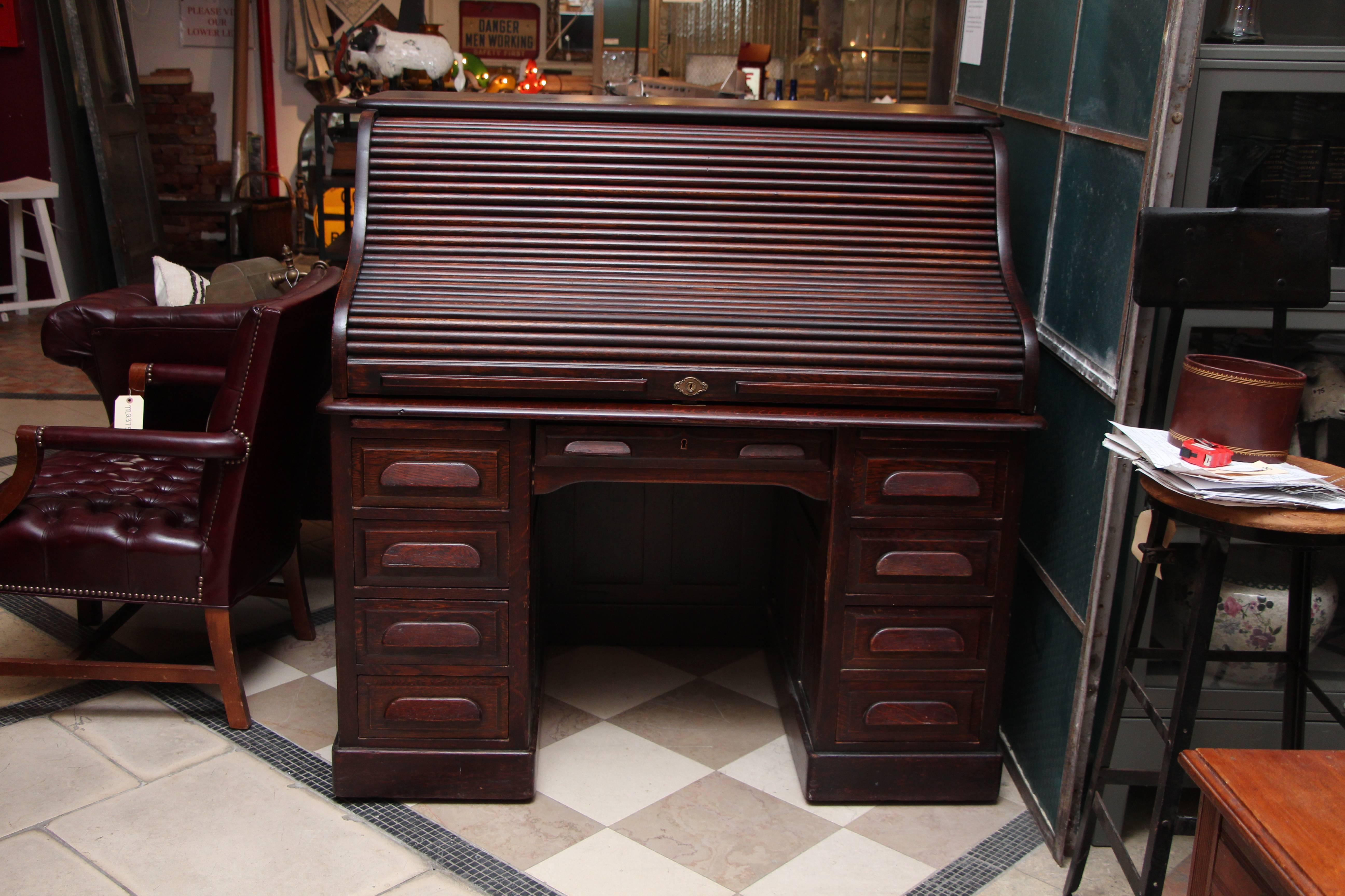 1910s petite antique wooden serpentine roll top desk with nine drawers. This antique desk is quarter sawn oak and finished with a dark mahogany finish with original hardware.  Detail is excellent with slotted interior and divided drawers. Raised