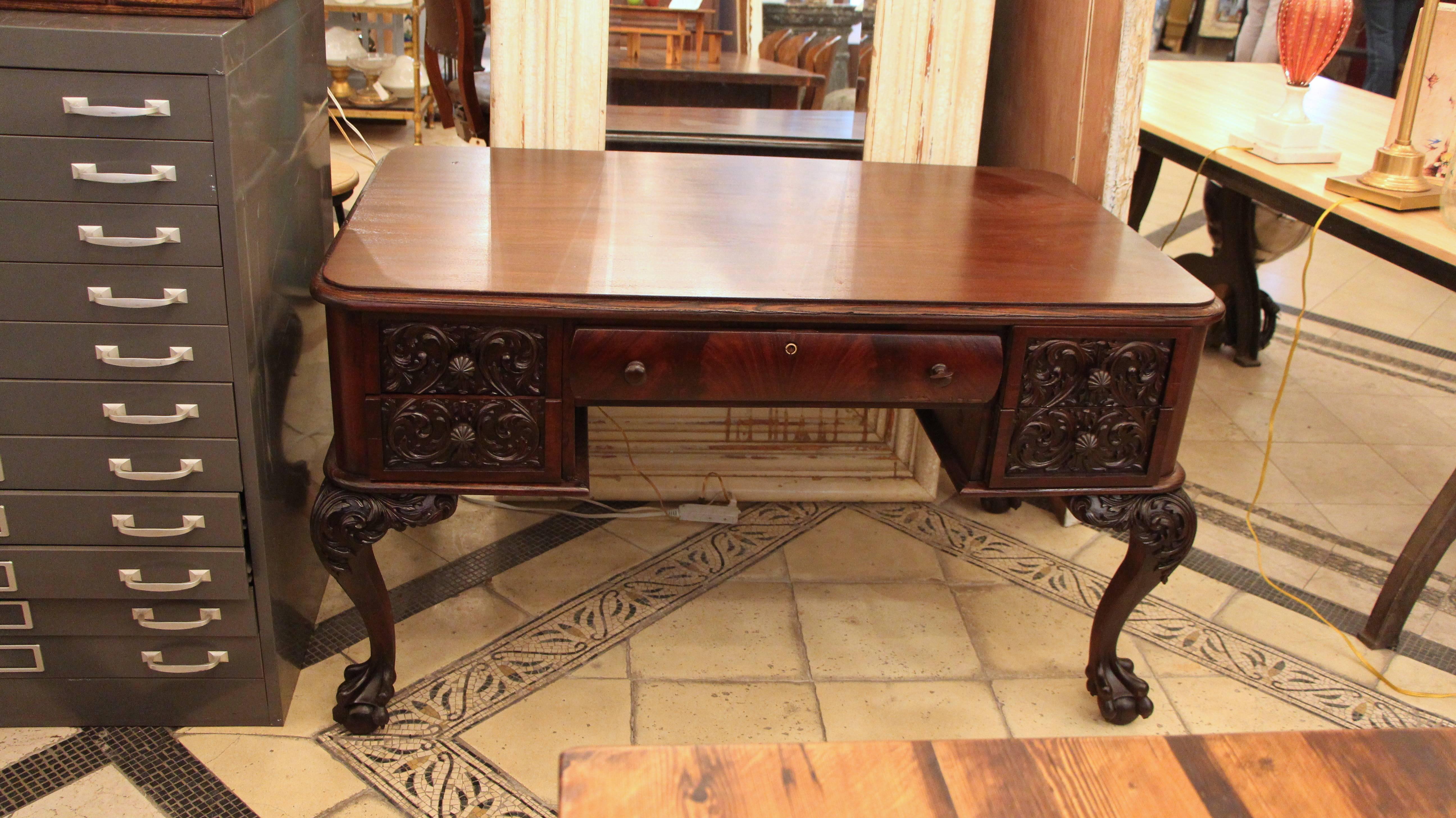 1910s petite flame mahogany carved desk with claw feet in overall great condition, with very minor imperfections in the veneer. Recently restored. One small piece missing on one carved foot and part of one of the carved pulls. This item can be