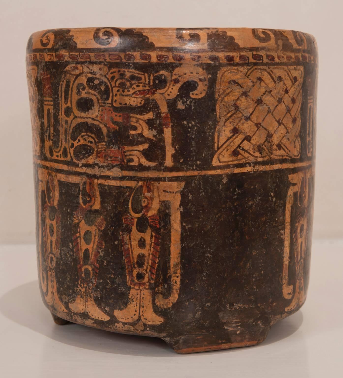 Pre-Columbian, Honduras, Ulua Valley, polychrome pottery cylinder on three nubbin feet painted in shades of red, orange and black. With upper raised band with reateating series of stylized wave glyphs. Lower section painted with two repeated panels,