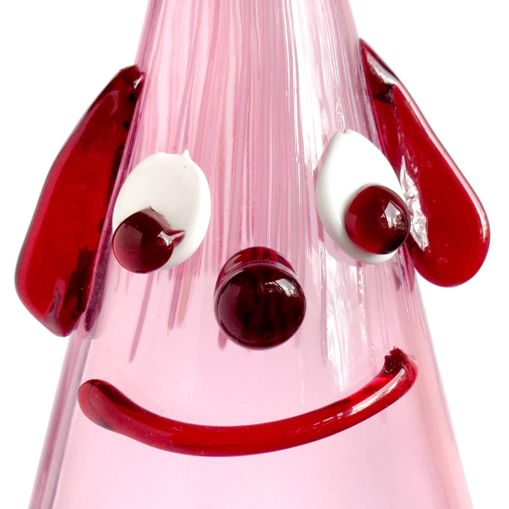 Cute and unusual Murano hand blown Italian art glass cranberry pink decanter, with applied red and white clown face. Documented to the Fratelli Toso Company. The piece has droopy ears, wide eyes, a big smile and threads of pink glass for the hair.