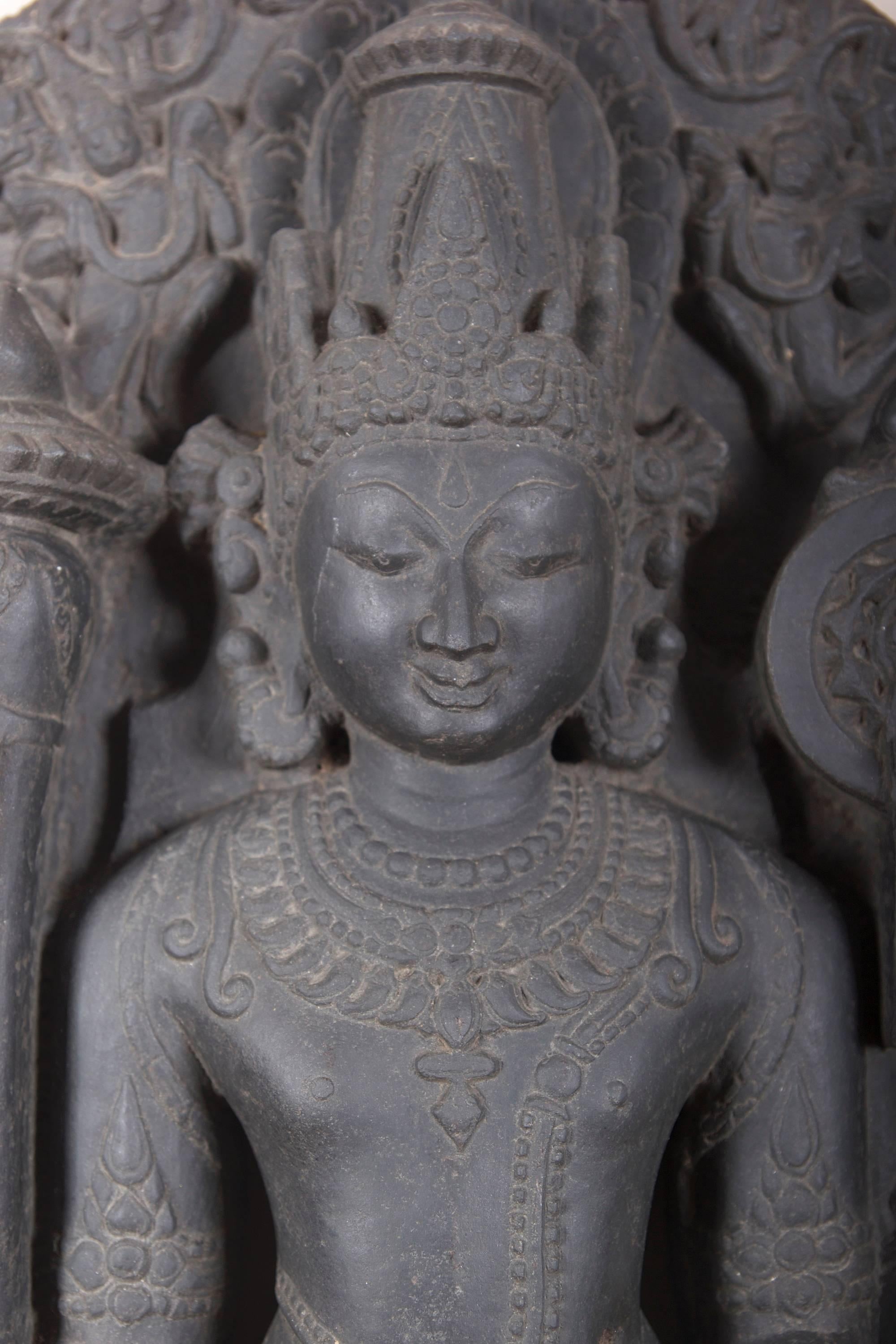 A carved figure of Vishnu standing in samapadasana, holding a lotus, mace chakra and conch, dressed in a short striated dhoti and embellished with various necklaces and bracelets. The serene countenance has a bow-shaped mouth and elongated eyes,
