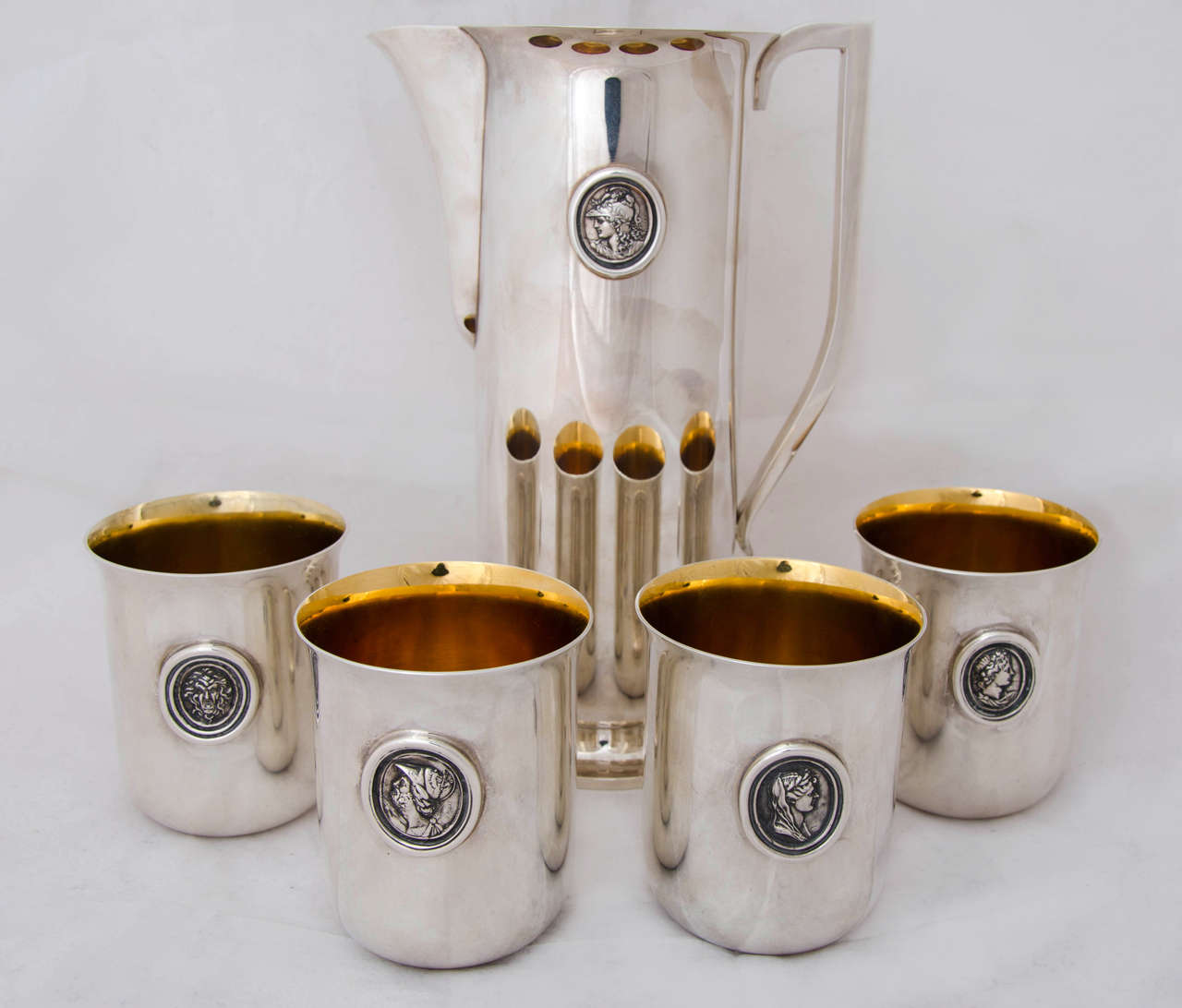 An English sterling silver water pitcher and four beakers. Each piece is applied with a silver cast of antique wax seals made from neoclassical intaglios by the English gem engraver Nathaniel Marchant R.A. 1739-1816. The design of the beakers and