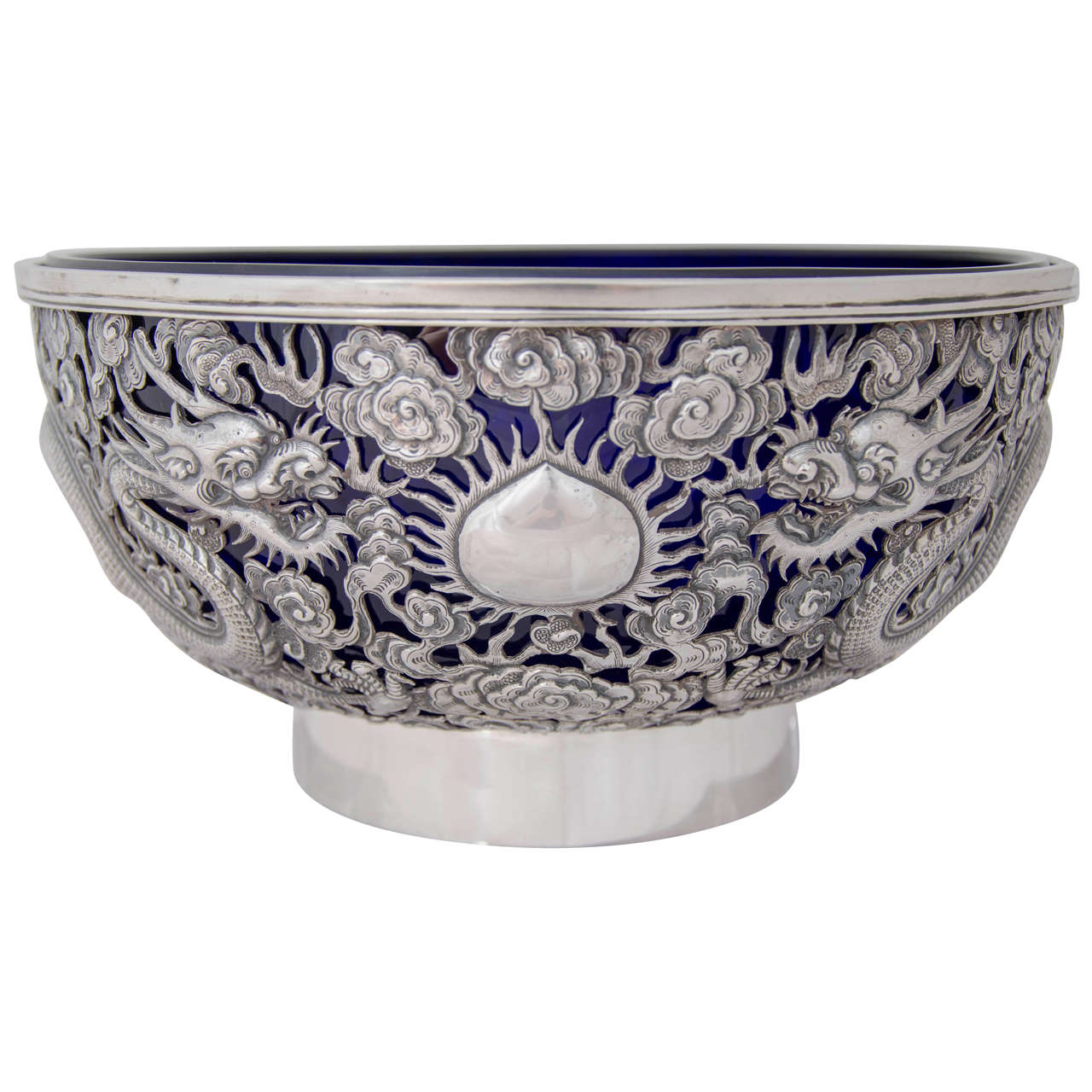A Large Chinese Export Silver Bowl circa 1890, beautifully pierced with 2 opposing dragons separated by a flaming pearl, and a third dragon breathing fire, and with a blue glass liner. 
Marked WH for Wang Hing '宏兴‘ which was the largest silver