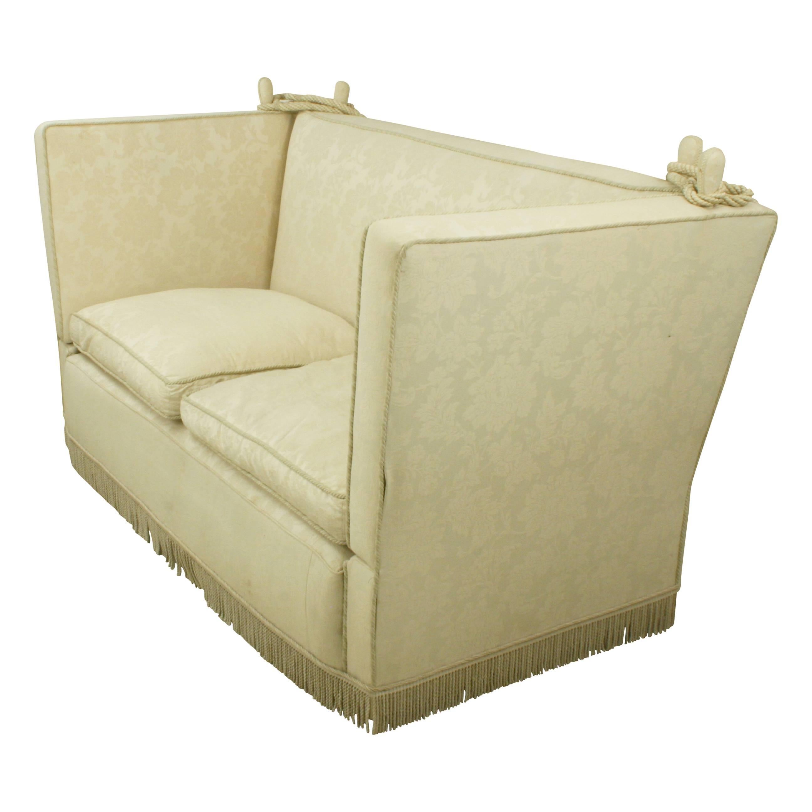English Knole sofa.
A large two-seat Knole settee with adjustable arms, deep seating, cream fabric with fringing. The traditional Knole settee is raised up on castors with drop arms and heavy decorative braid tie backs with elaborate tassels and