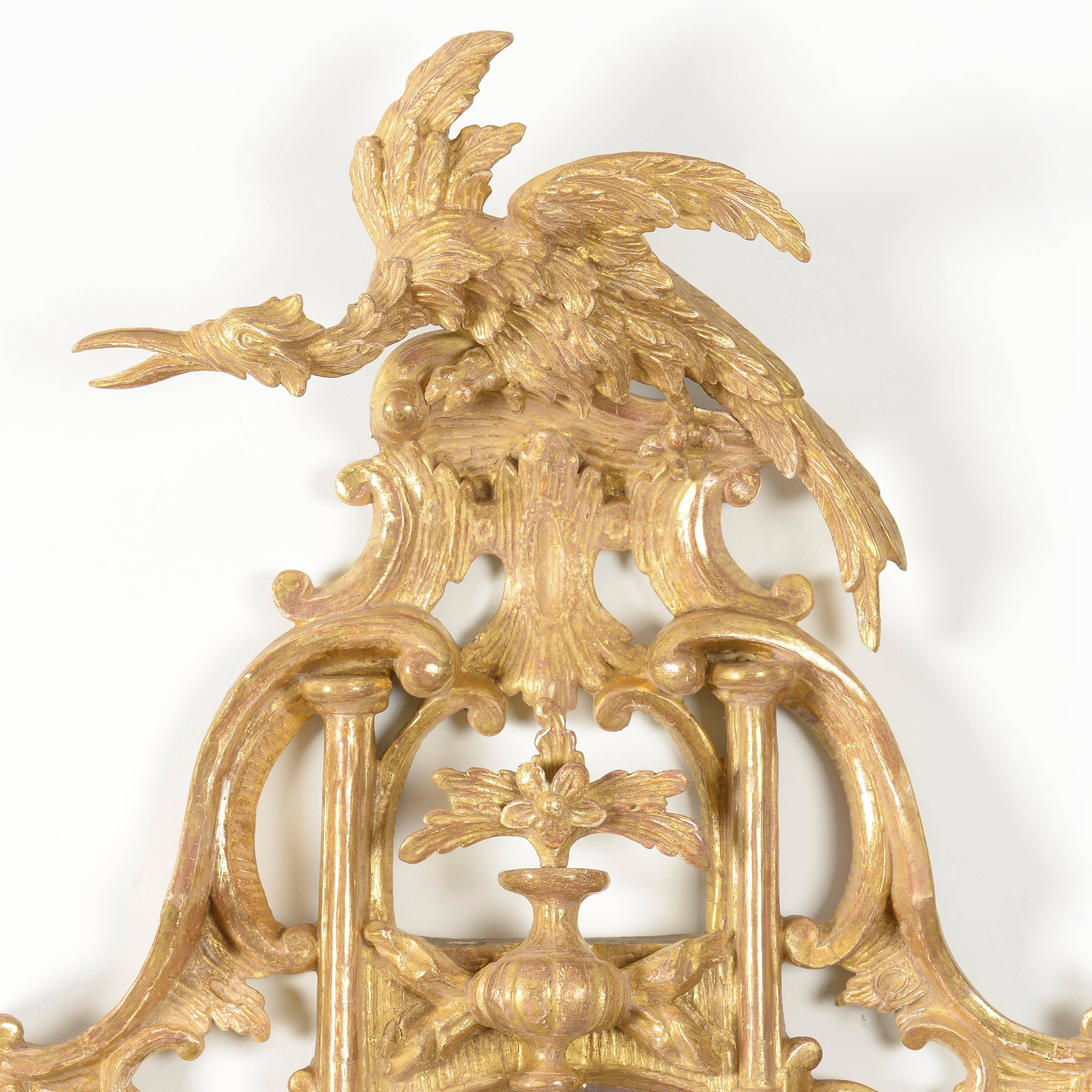 A superb pair of George III carved giltwood oval mirrors. The crest in the form of a Ho-Ho bird sitting on an acanthus carved perch support by columns and a shaped urn. The oval silvered plates are bordered by a carved frame with pierced scrolls and