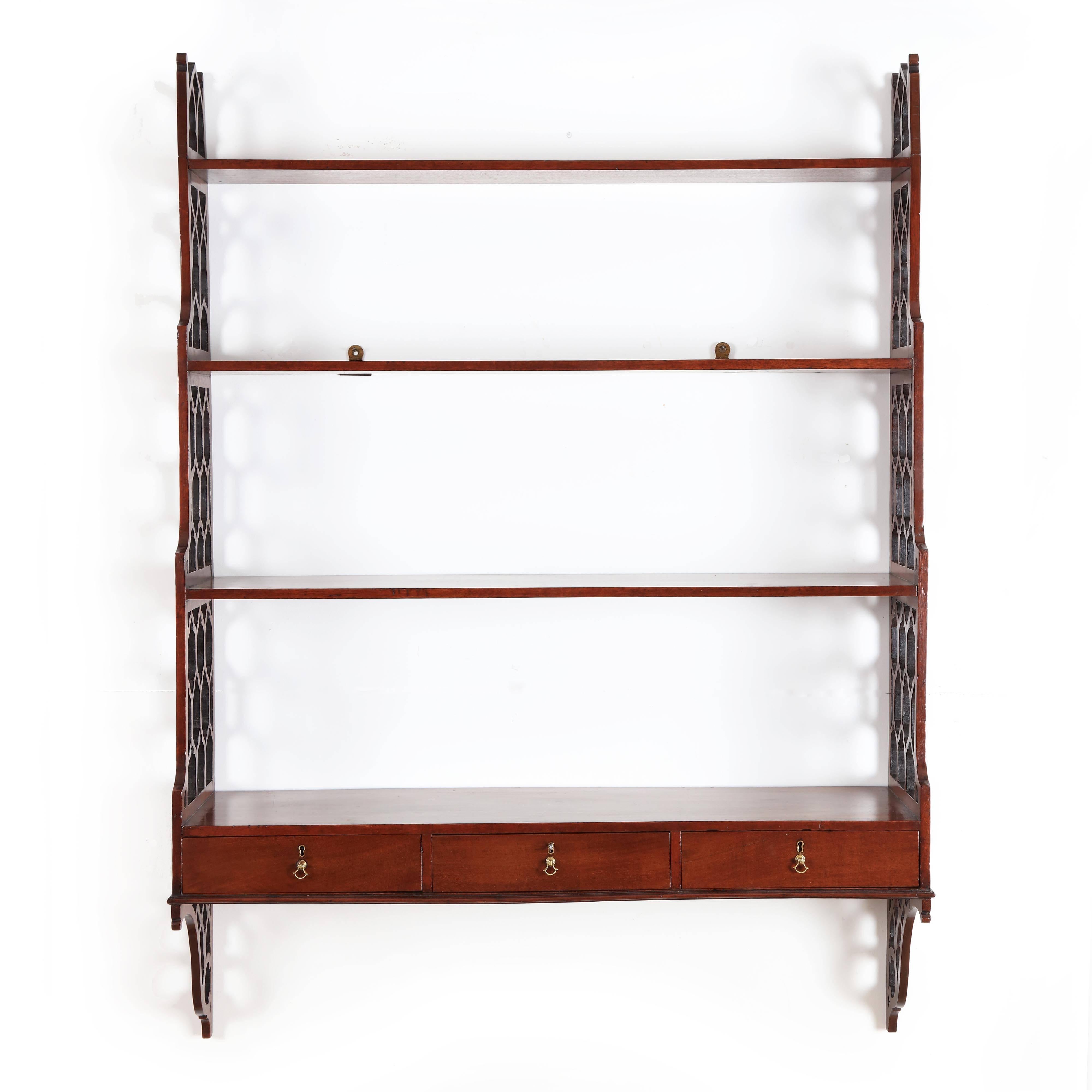 An important set of George III Chippendale period mahogany hanging wall shelves. The pierced fretwork fashioned sides in the Chinese Chippendale taste. The sides are joined by three horizontal shelves and an integrated bottom frieze section with a