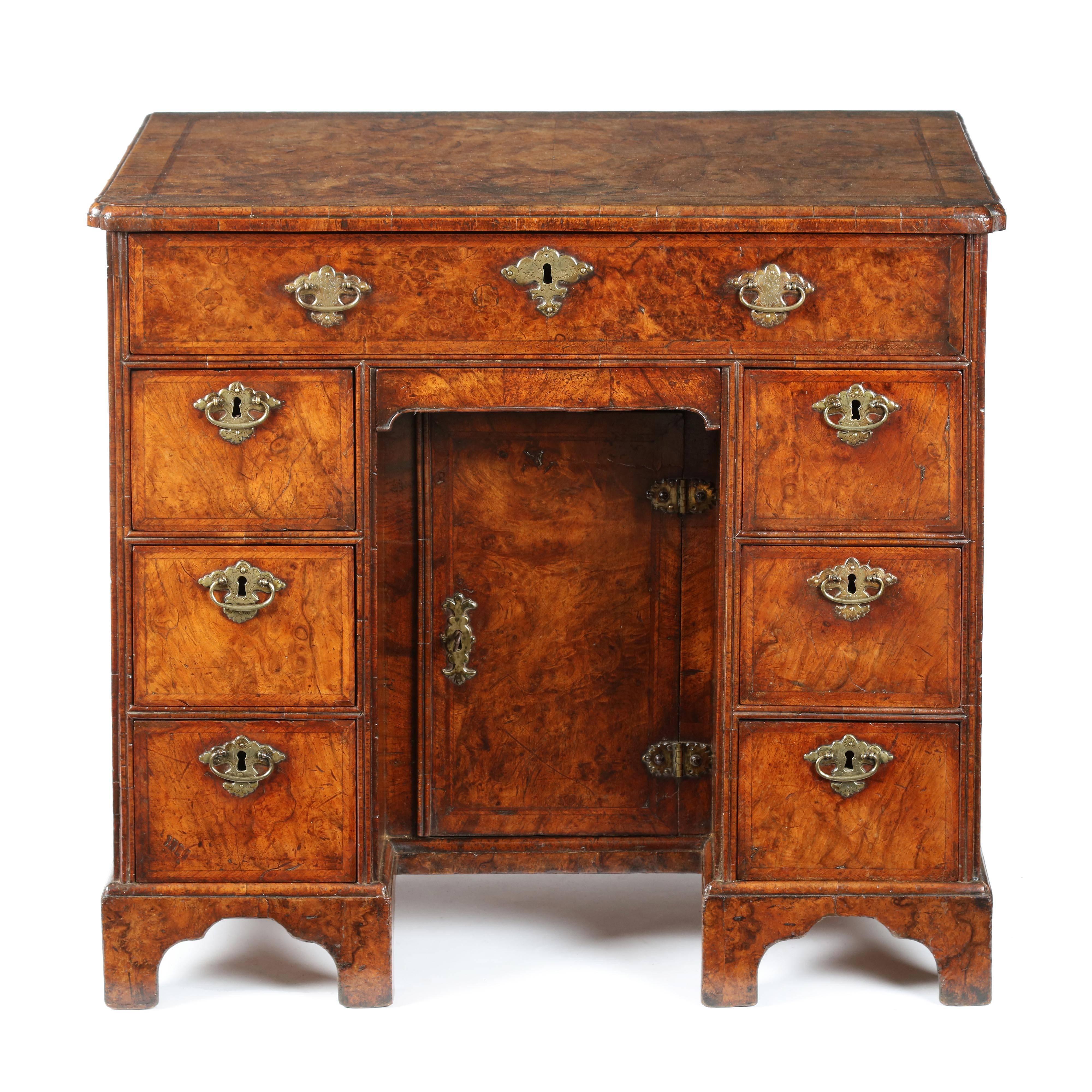 A superb, rare Queen Anne burr walnut and feather banded kneehole desk with secretaire top drawer, retaining excellent original color and patina. The rectangular top, quarter veneered, feather banded with a moulded edge and front re-entrant corners.