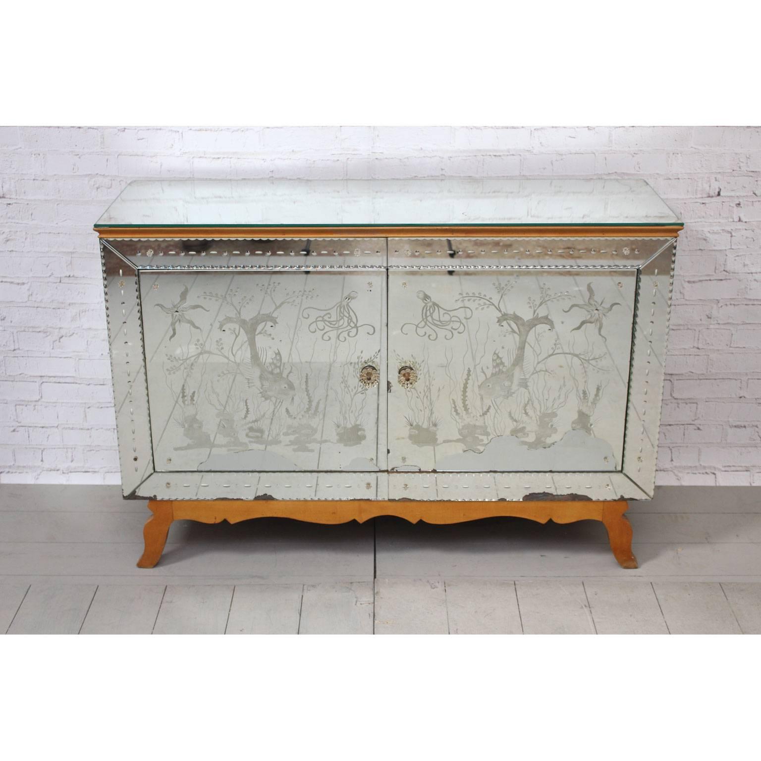 This charming mirrored sideboard, which has a lovely glow about it is decorated with etched fish, octopi, starfish and sea life. The mirror which covers the top and sides as well as the front is beautifully aged. Every detail is considered down to