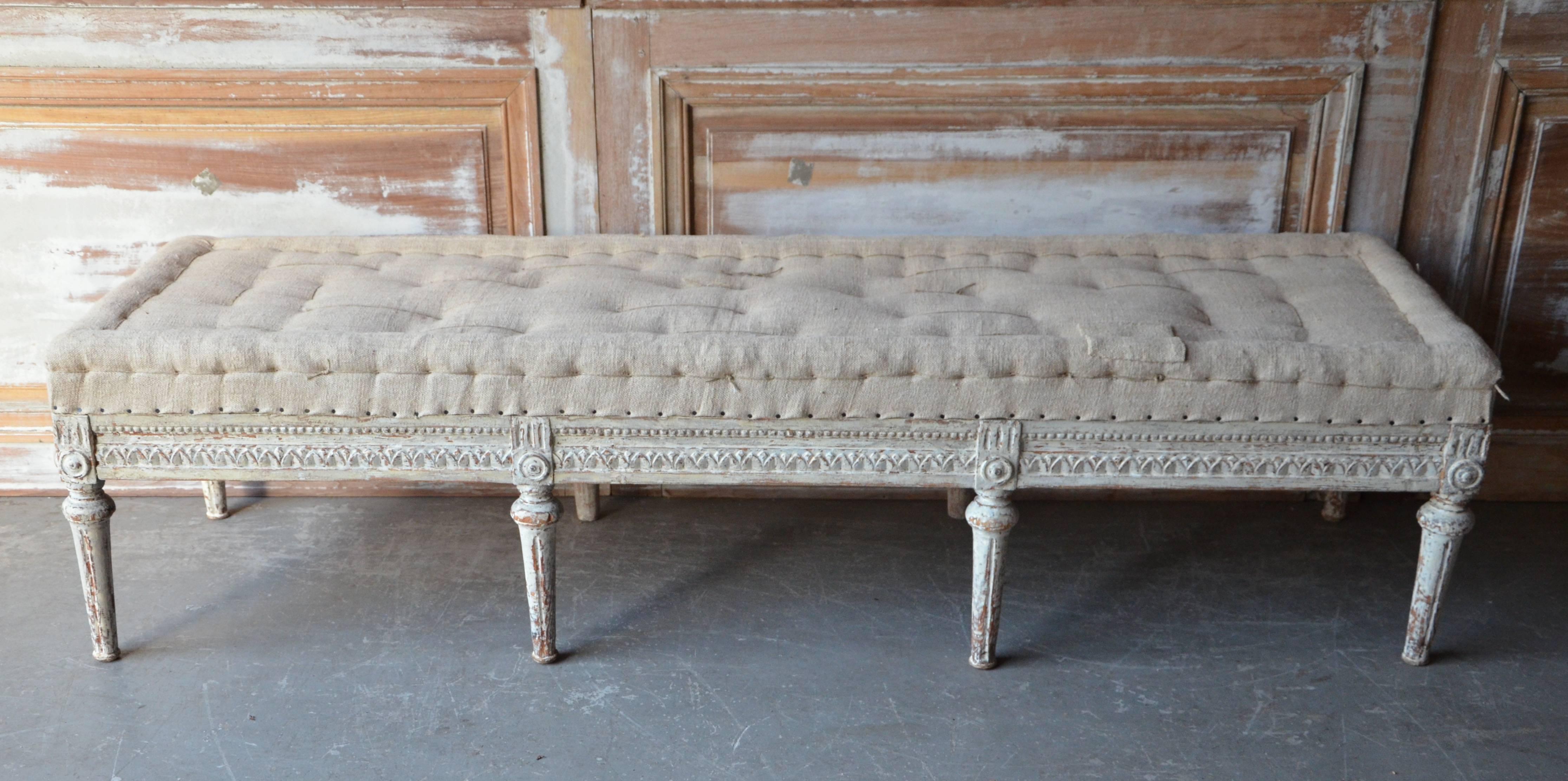 Swedish period Gustavian bench, circa 1800, finished on three sides with leaf rod and rosette carvings on carved round fluted legs. Scraped to original cream white finish and upholstered in traditional way in antique hand-stitched linen. Timeless
