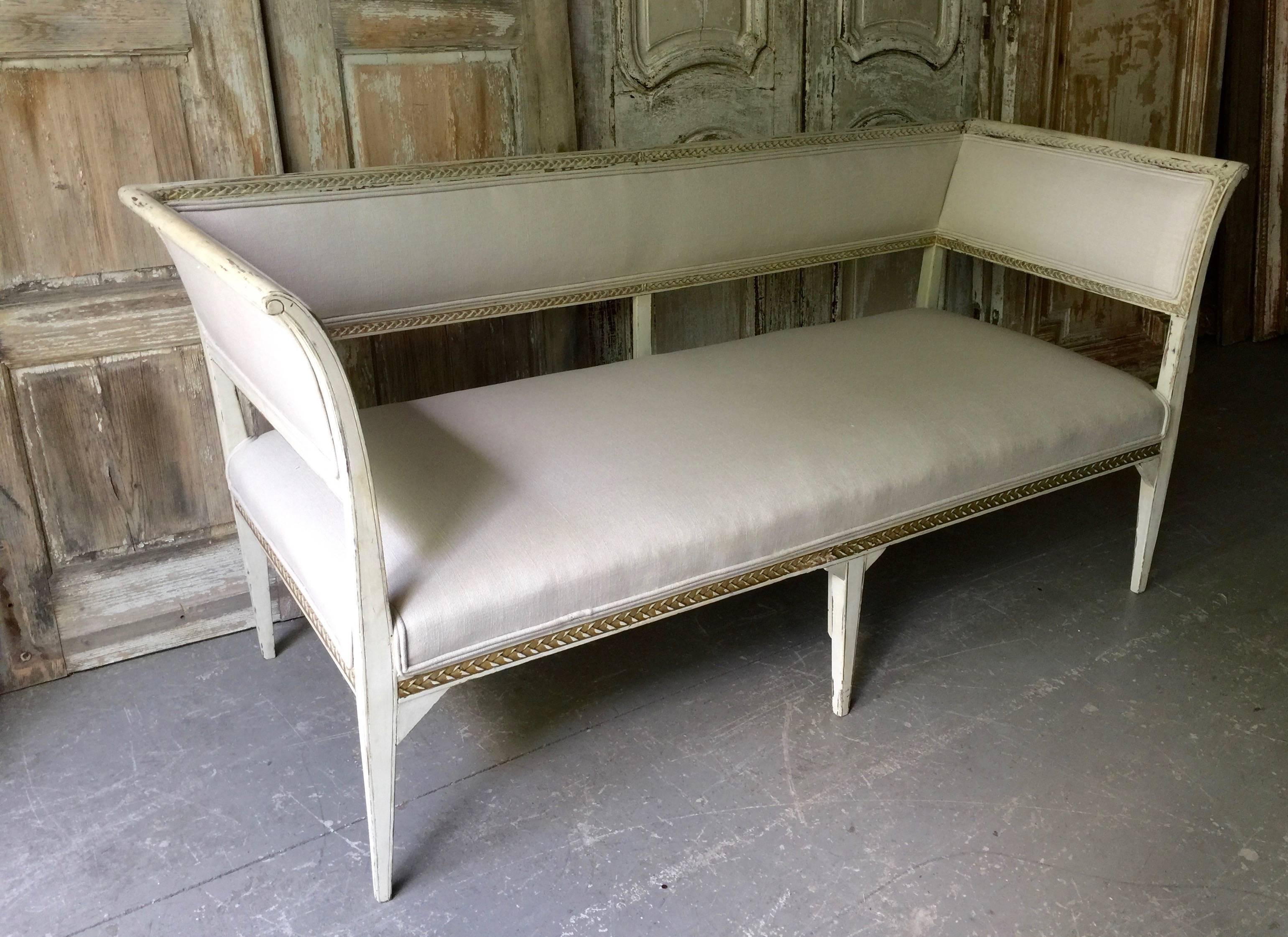 Late 19th century Swedish Gustavian style sofa with richly carved backrest and sides with traces of gold gilt accents. Reupholstered in hint of palest gray tone linen. 
Seat size: 55