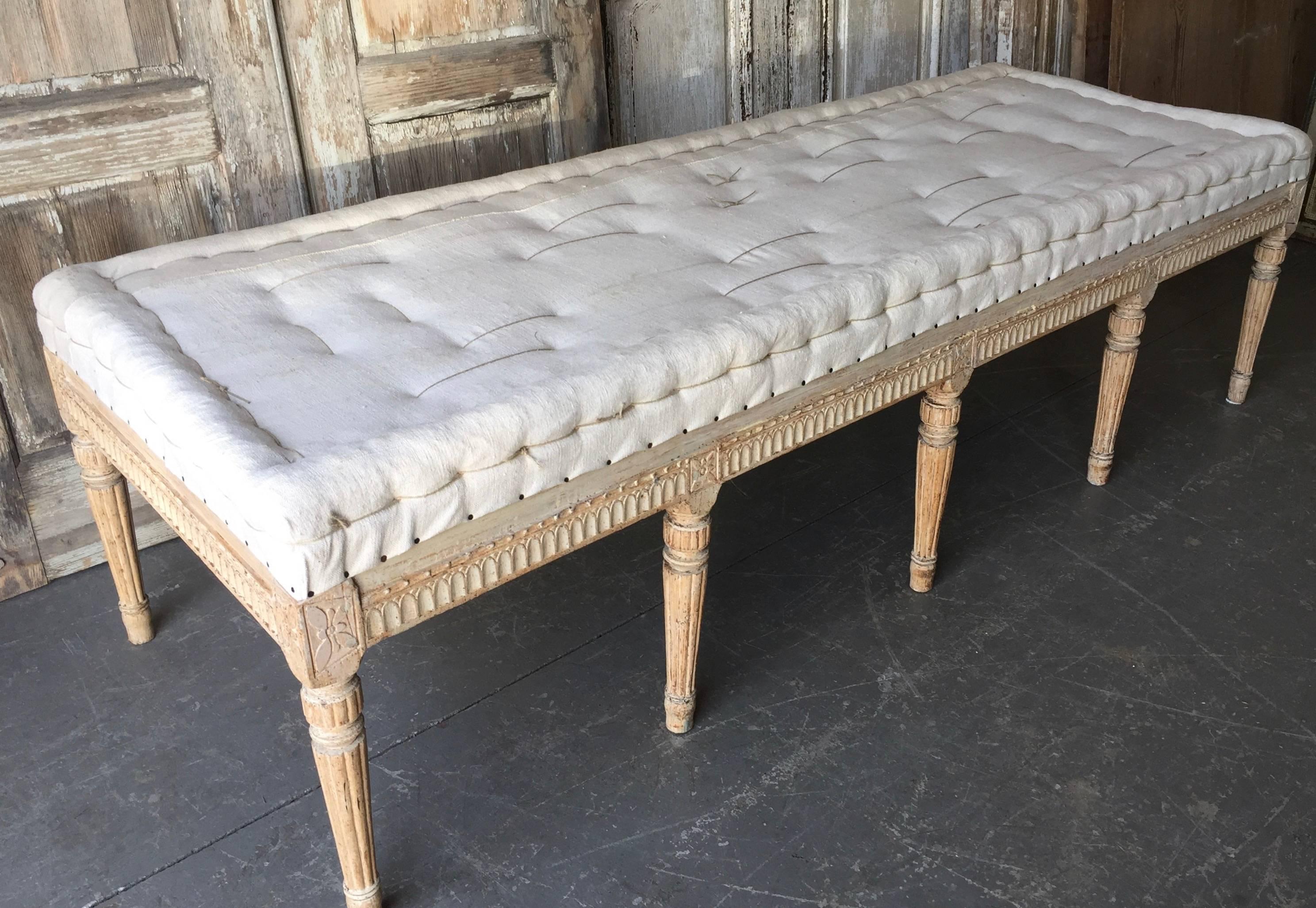Swedish Gustavian period bench, circa 1800, finished on three sides with leaf rod and rosette carvings on carved round fluted legs. Scraped to original cream white finish and upholstered in traditional way in antique hand-stitched linen. Timeless