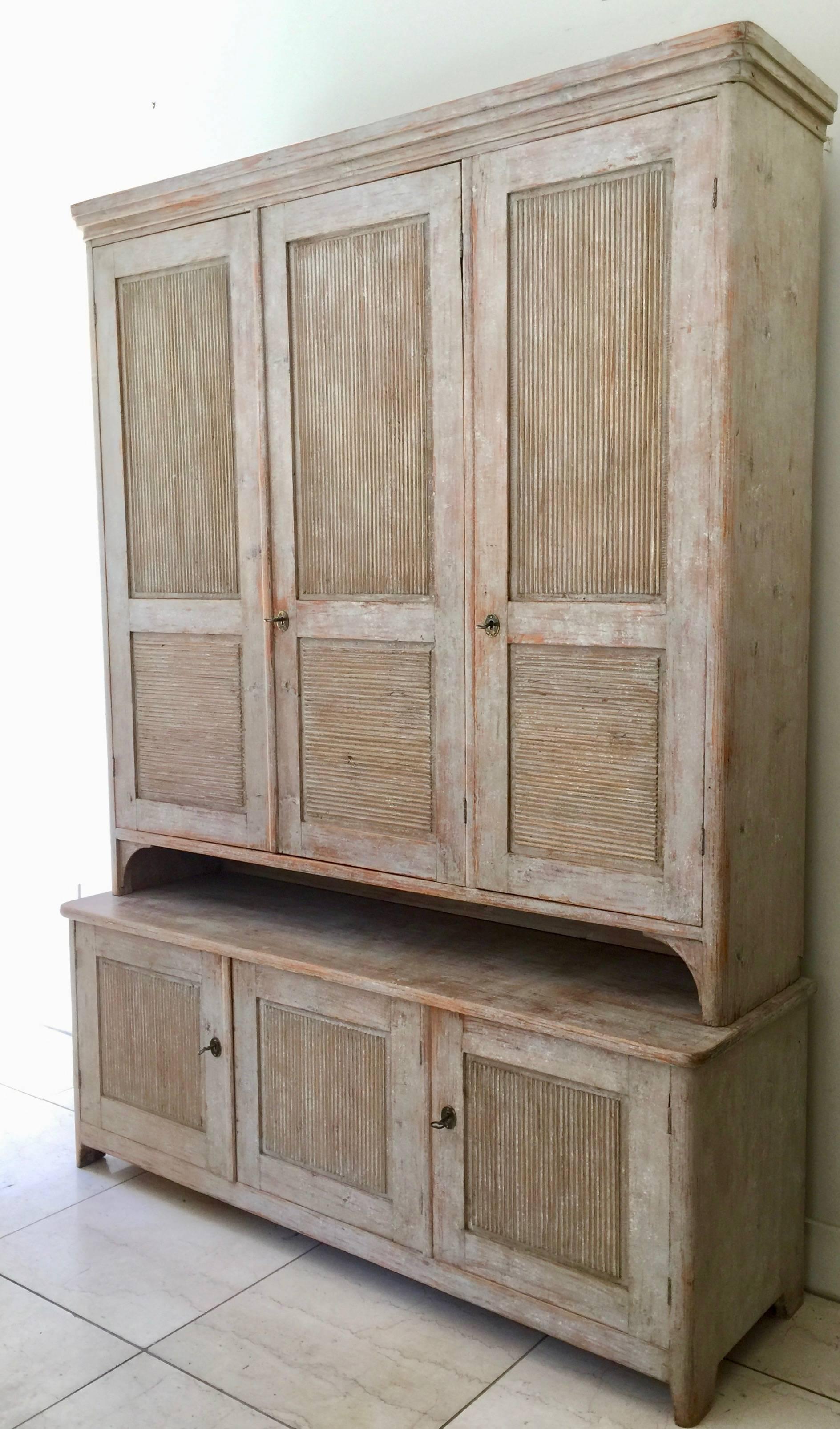 An exquisite and large, period Swedish Gustavian cabinet, in two parts displays Classic Gustavian styling with six reeded door panels in wonderful worn cream white patina scraped back to its original paint. Very practical with plenty of