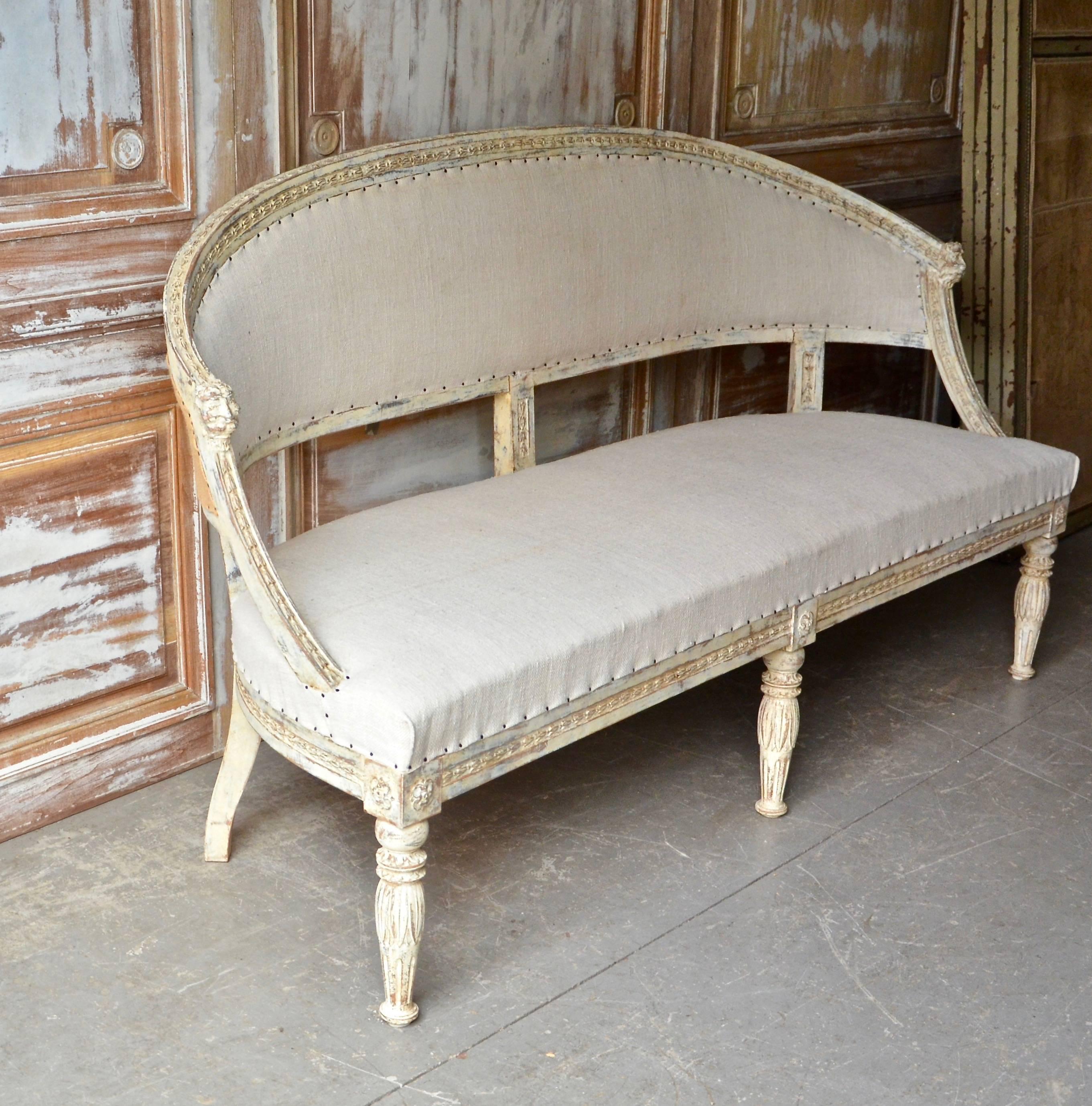 Swedish, 19th century barrel back sofa settee with beautifully carved frame with bell flower and lion's heads carvings. Richly carved front legs with lotus flowers and rosettes. Scraped to original paint and upholstered in antique linen and