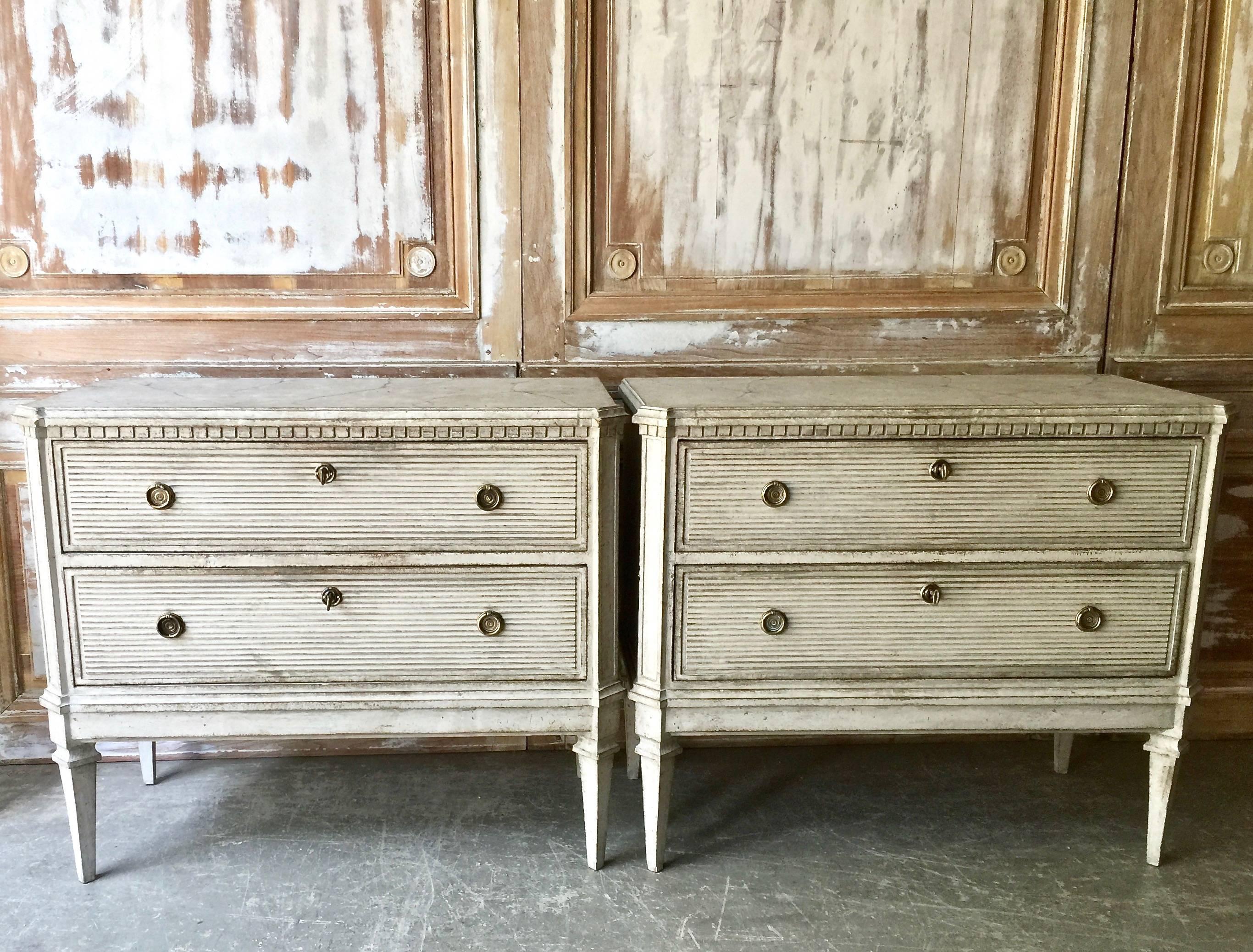 Pair of 19th century Swedish Gustavian Style two-drawer chests with horizontally reeded drawer fronts, dental trim, canted corner with carvings and tapering long square legs. Trace of faded marbling paint on the shaped top, 
Sweden, circa 1880.